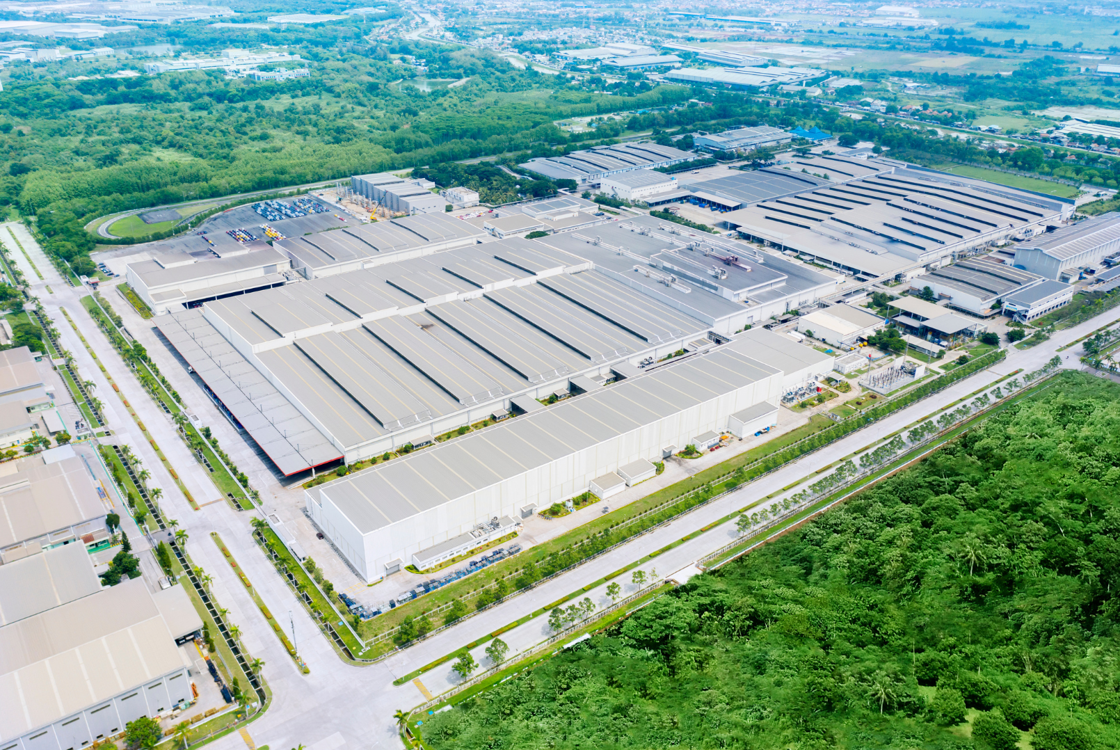 An aerial view of a large industrial complex surrounded by greenery, with multiple warehouses, roads, and parking areas.