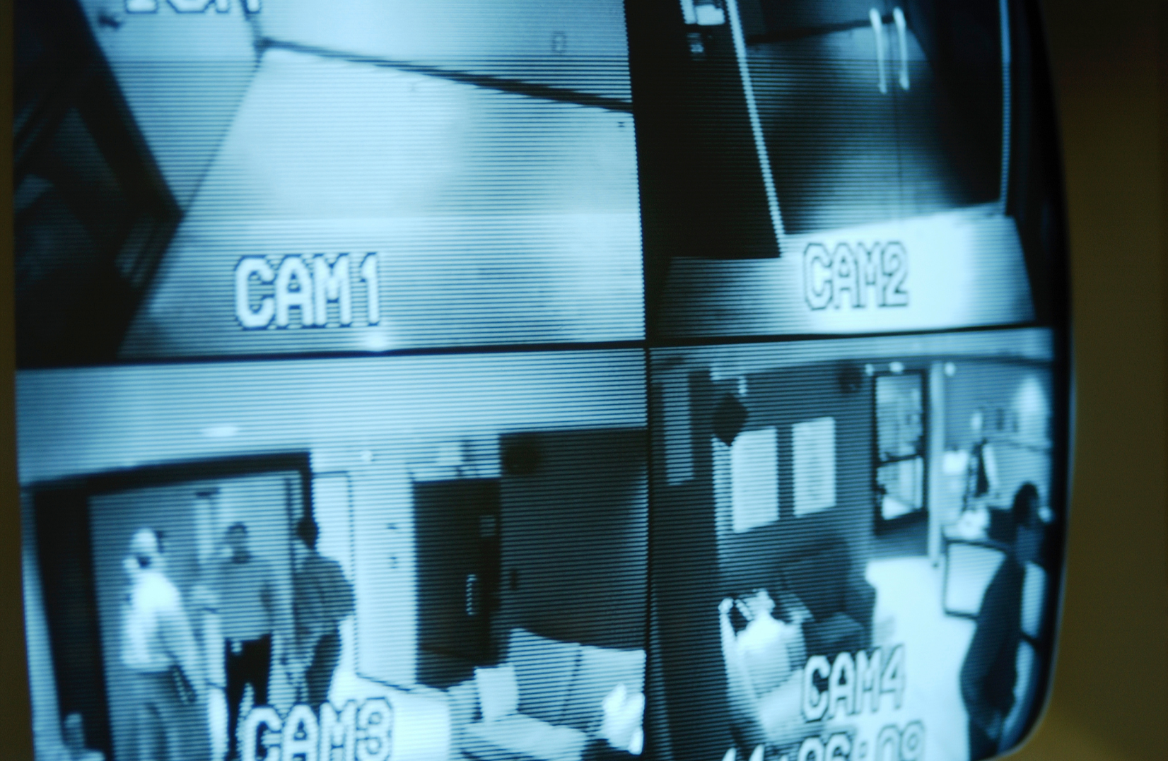 Black and white CCTV monitor displaying multiple camera angles of elevators and waiting rooms.