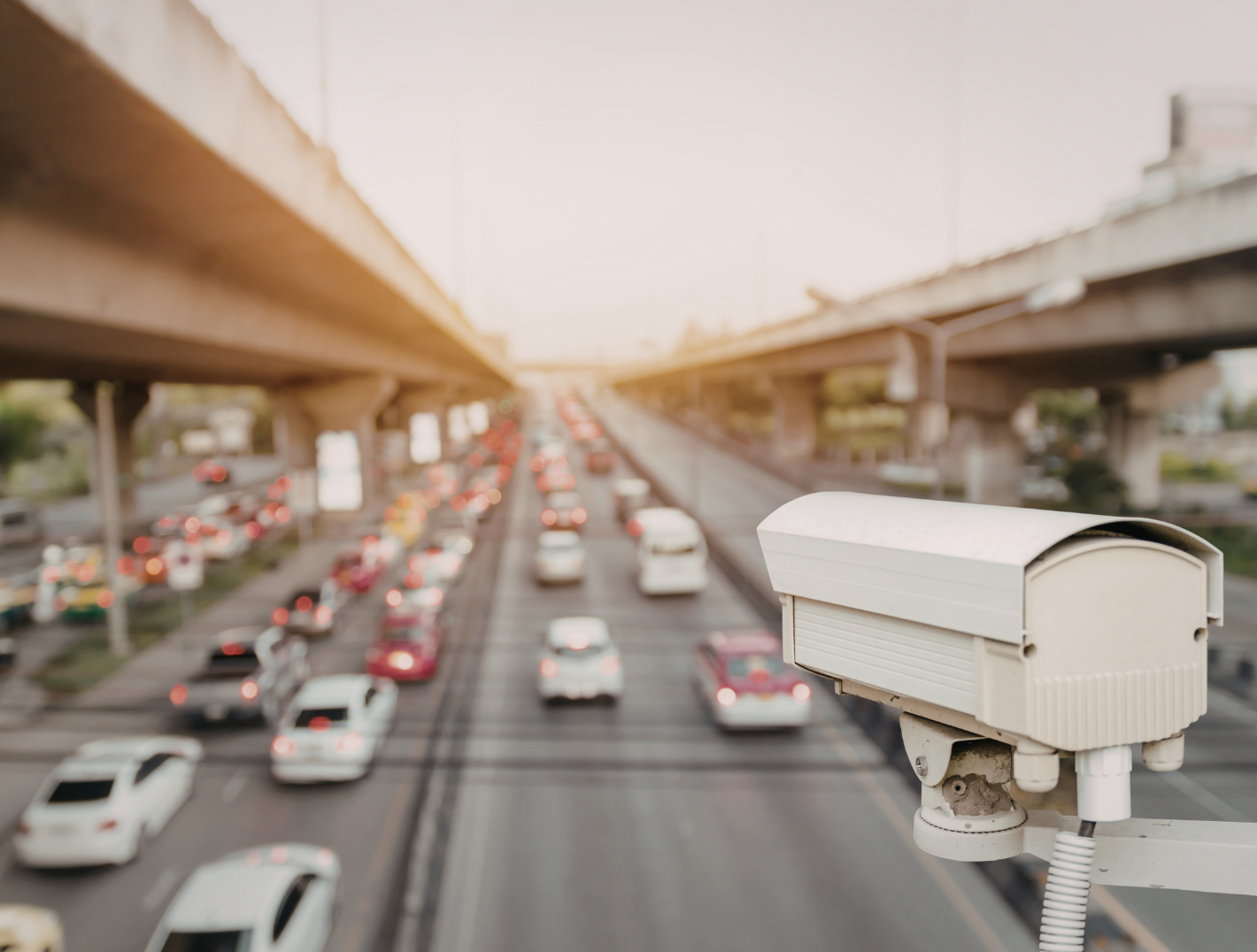 A security camera overlooking a busy highway with multiple lanes of traffic during sunset.
