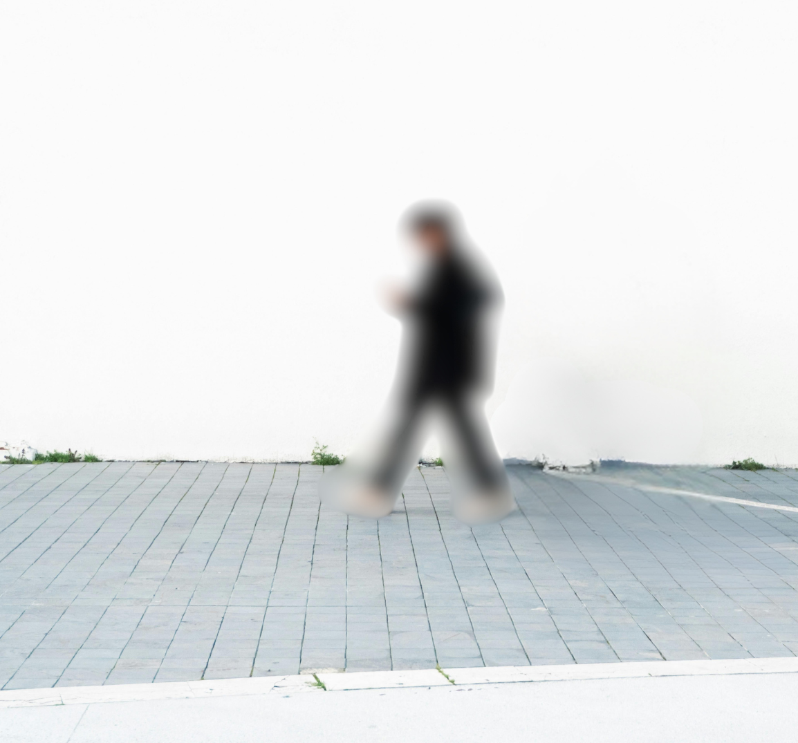 Person walking on a paved sidewalk and looking at a mobile phone against a plain white wall background.
