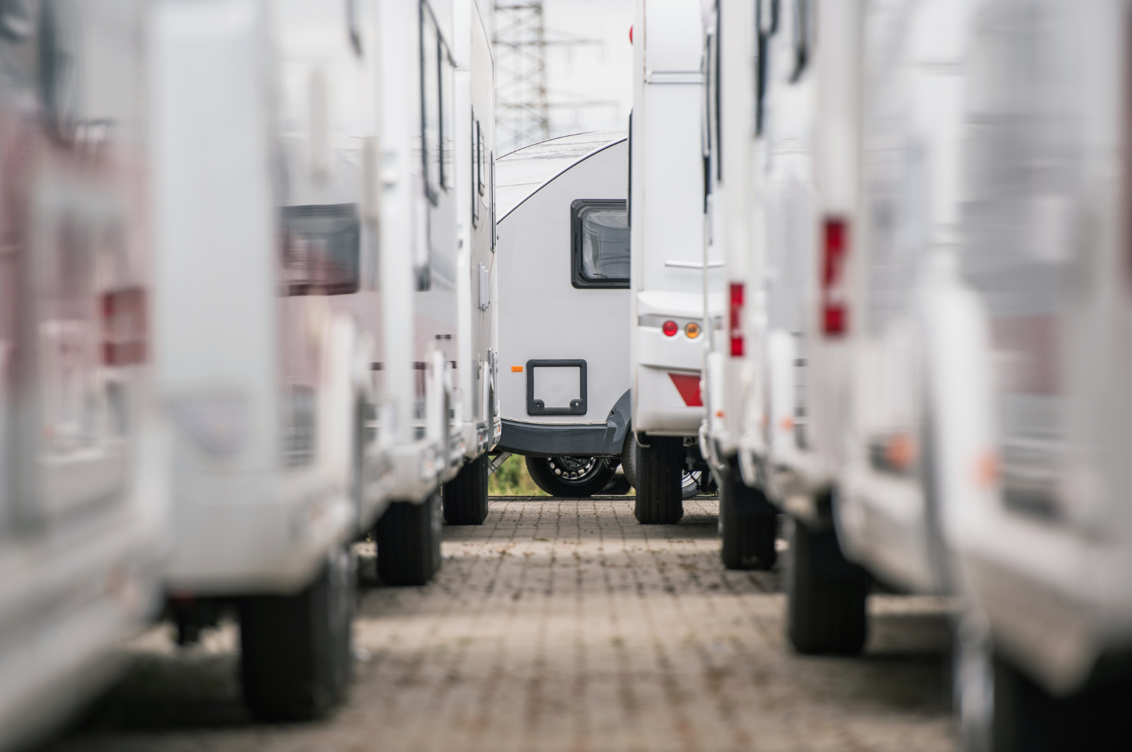 Multiple white recreational vehicles (RVs) parked on a paved lot, with a closer view of the wheels and sides and one RV in the background.