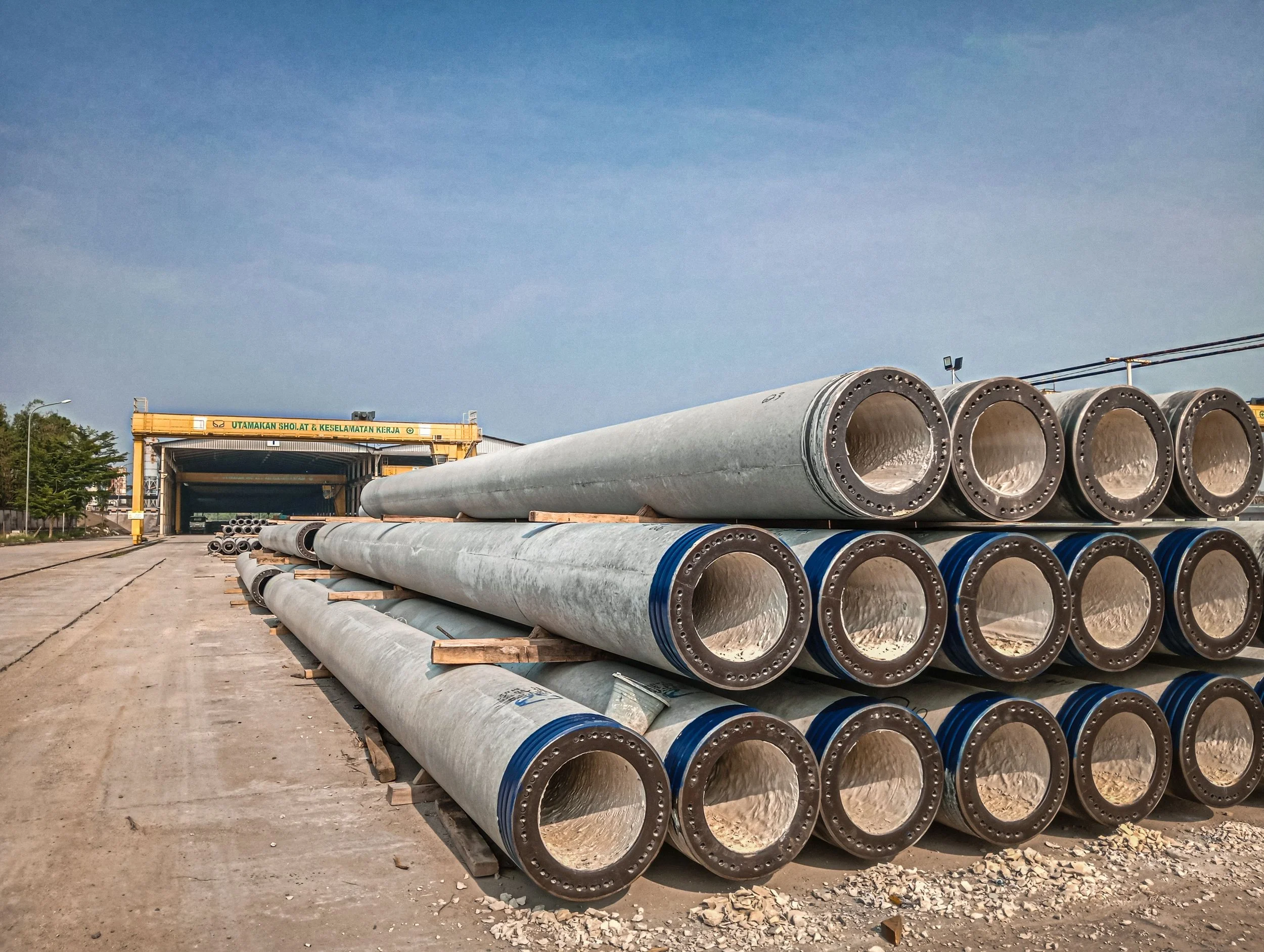 Large metal pipes stacked at an industrial construction site with a clear blue sky in the background.