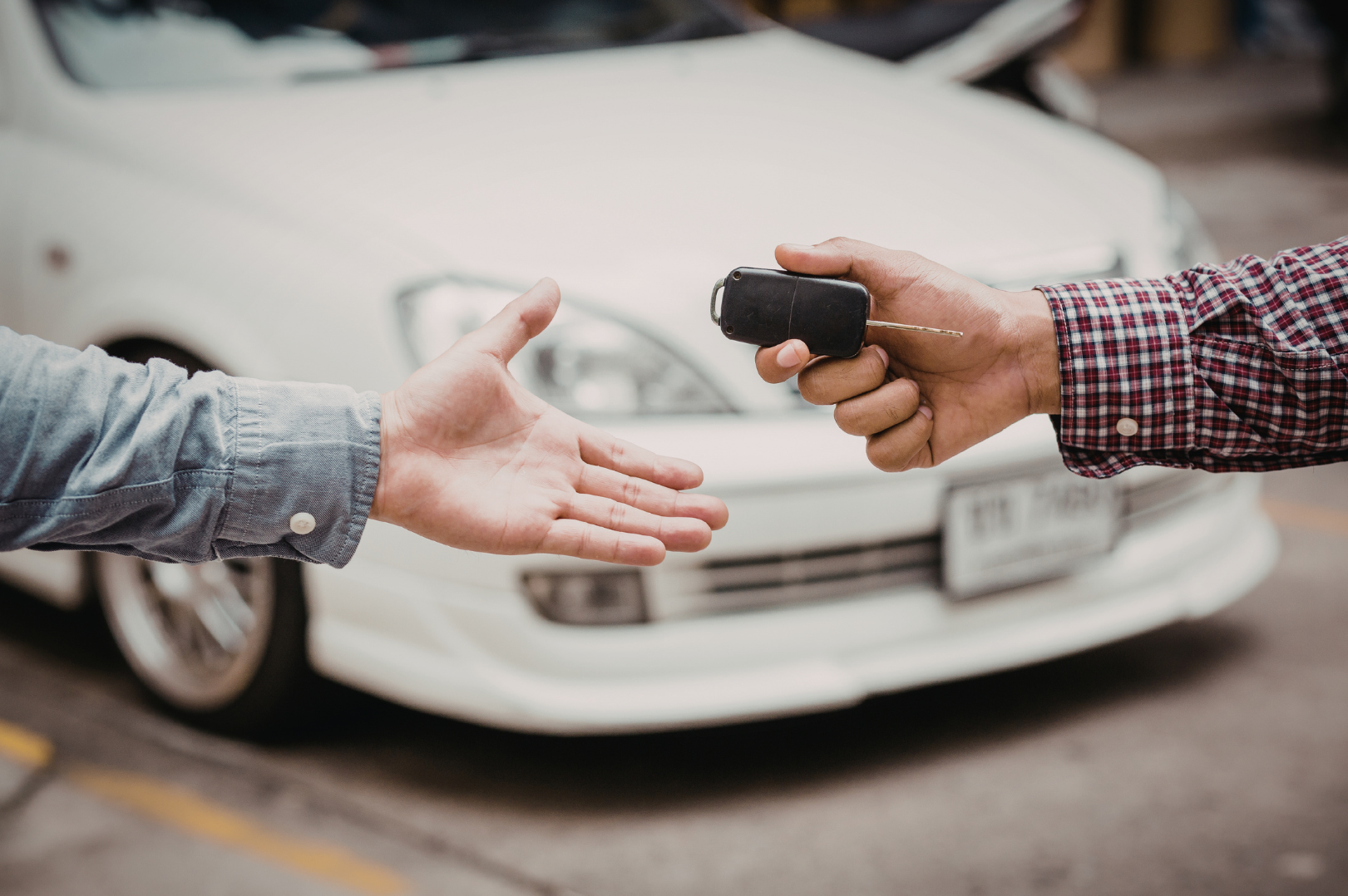 Person receiving car keys from another person in front of a white car in a parking lot.