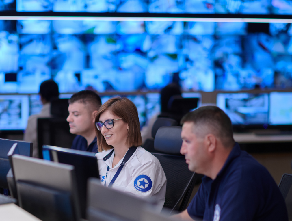 Security personnel working at a control room with multiple monitors displaying various images.