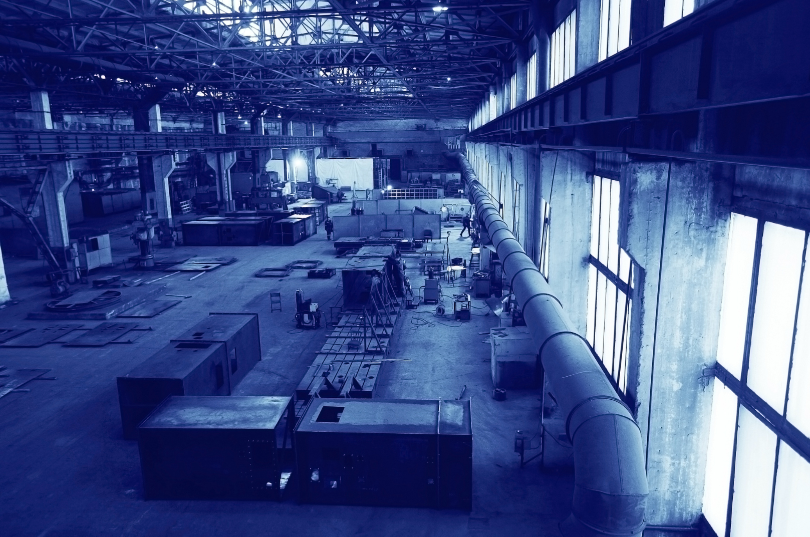 Interior view of an industrial factory or warehouse with high ceilings, large windows, and various machinery and equipment scattered around.
