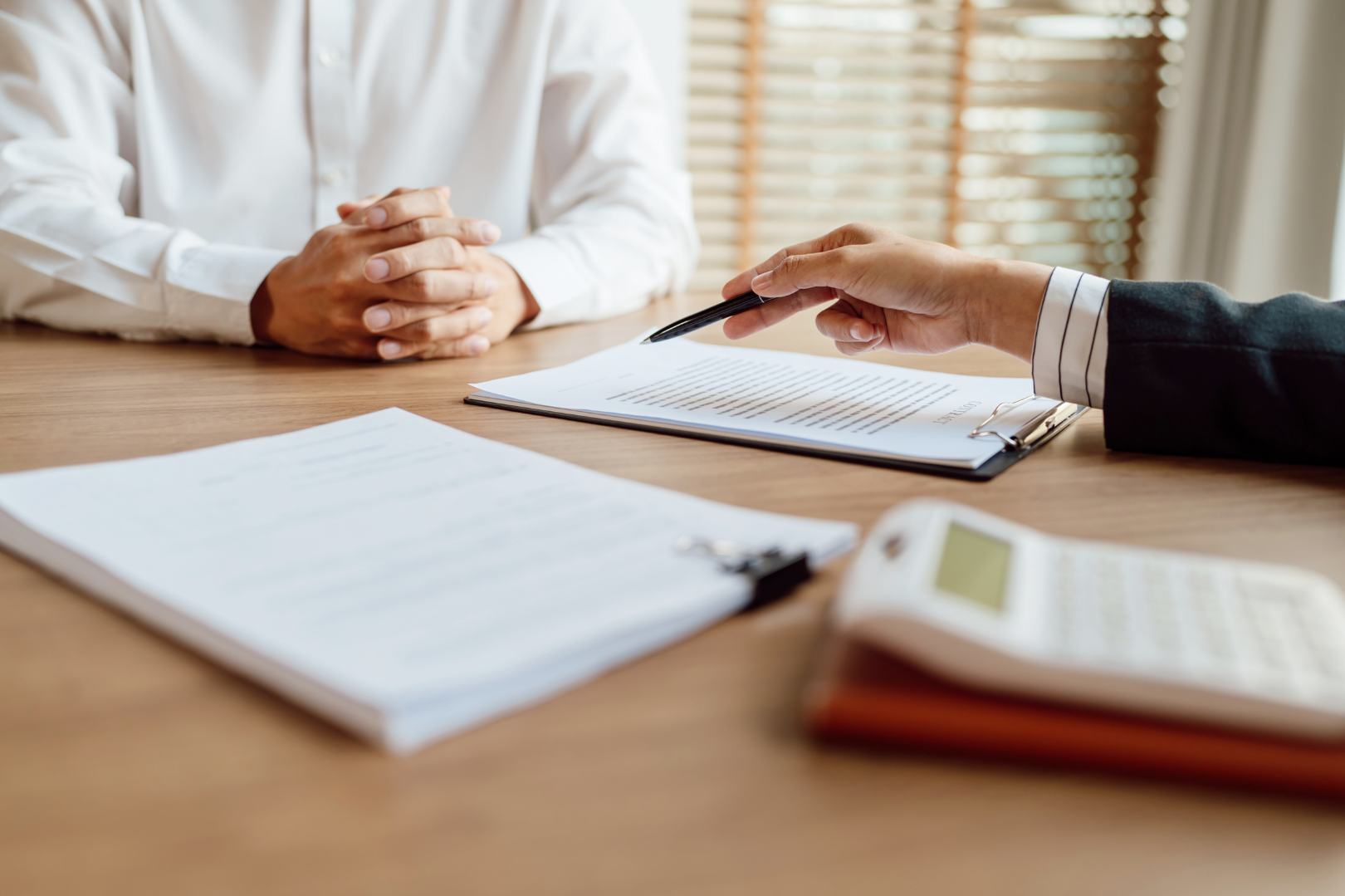 Two people having a business meeting at a desk, with documents, a calculator, and a pen.