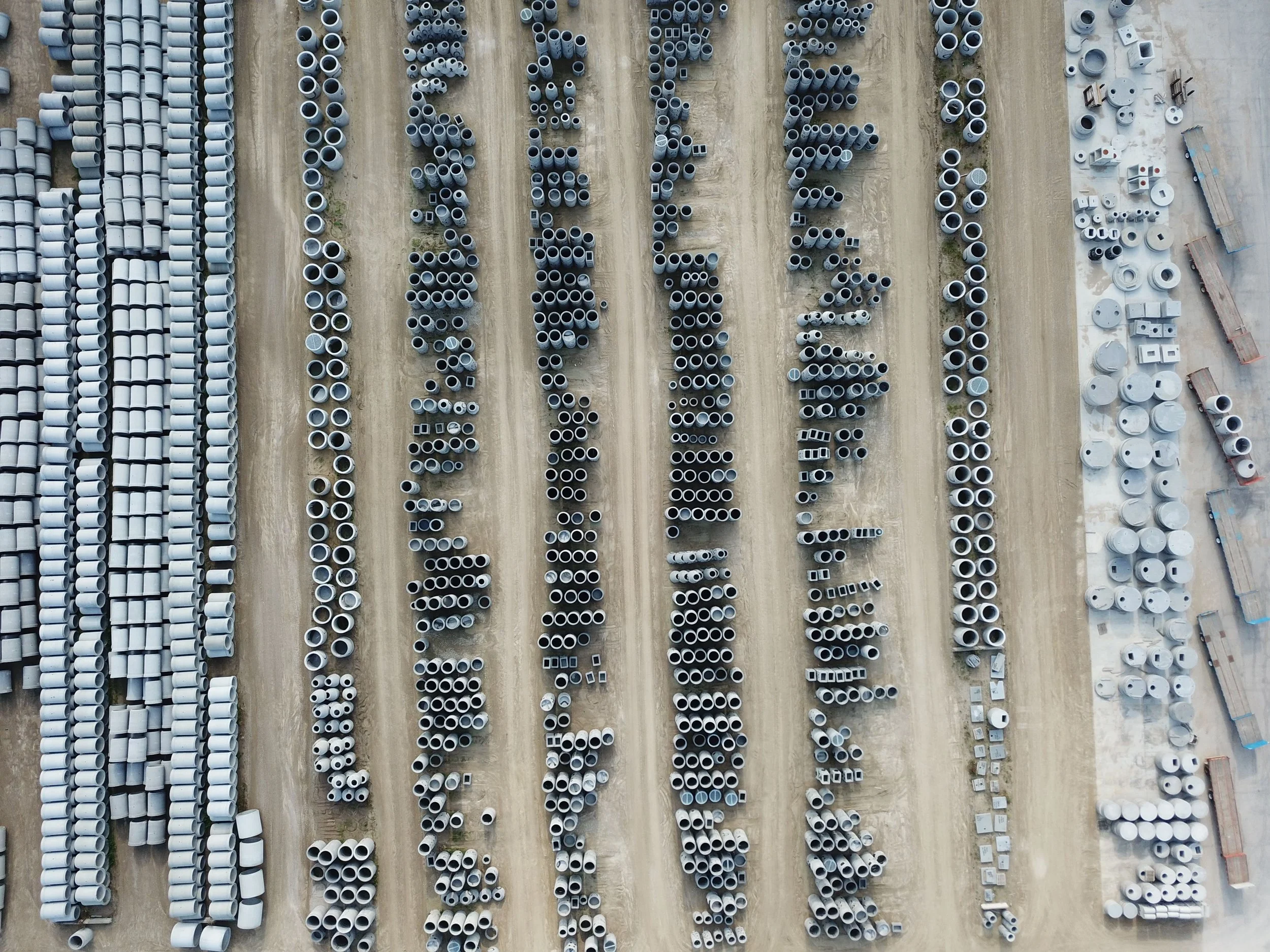 Aerial view of a large outdoor storage lot with rows of stacked gray pipes of various sizes, organized in parallel lines.