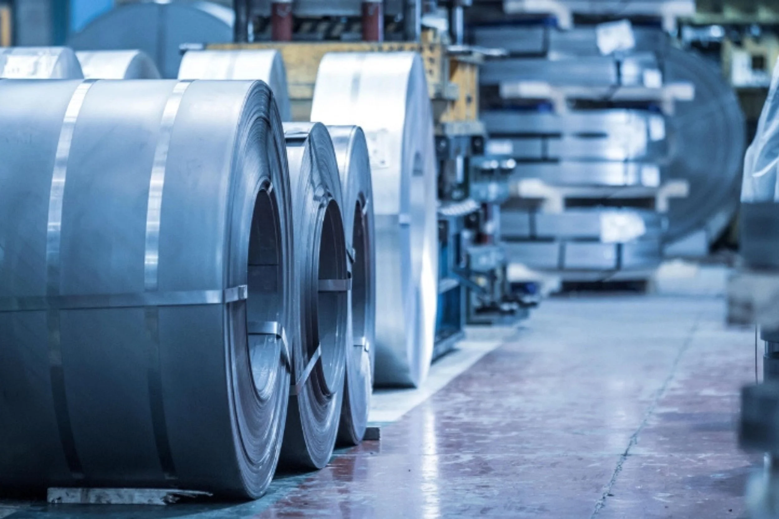 Industrial warehouse with large metal coils stored on a line, with additional machinery and supplies in the background.