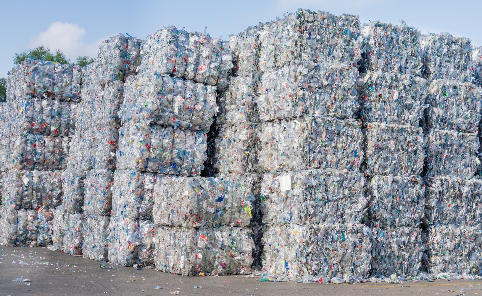 Large stacks of compressed recycling bales made of crushed plastic bottles at a recycling plant.