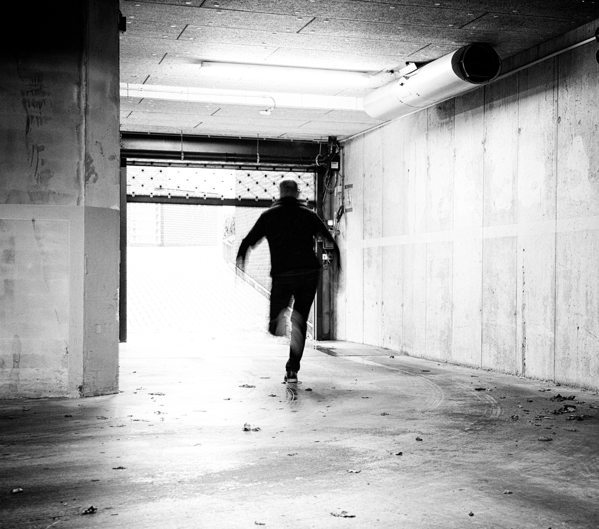 Person running through a parking garage or tunnel, captured from behind, in black and white.