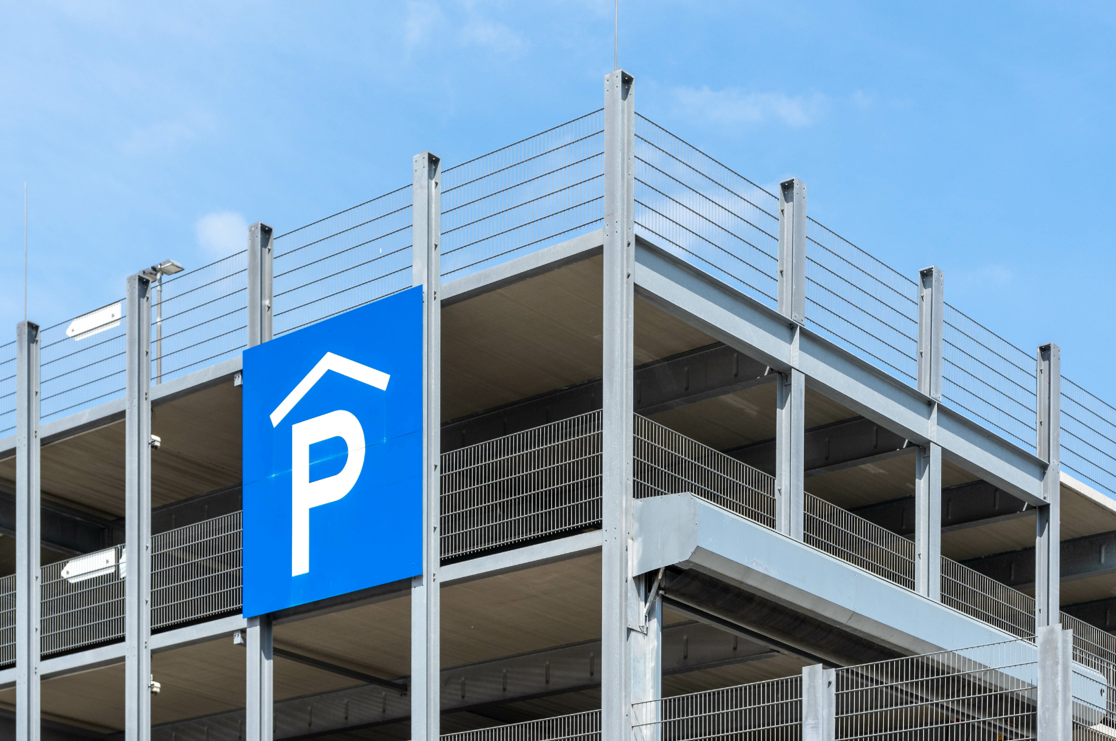 A multi-story parking garage with a large blue sign indicating parking, under a clear blue sky.