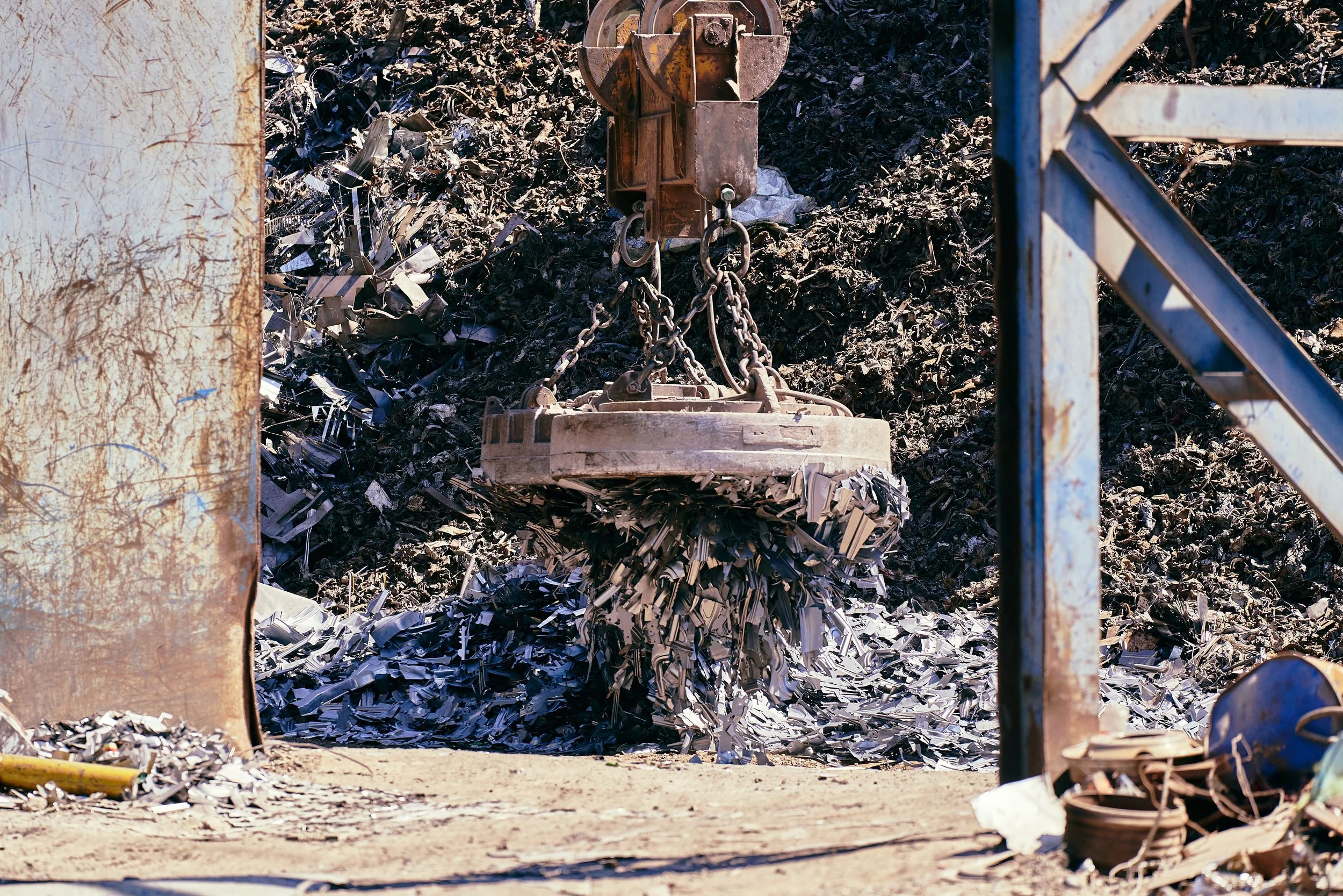 A recycling machine compacts shredded paper into a large roll of paper surrounded by piles of shredded paper. The scene appears to be at a scrapyard or recycling facility.