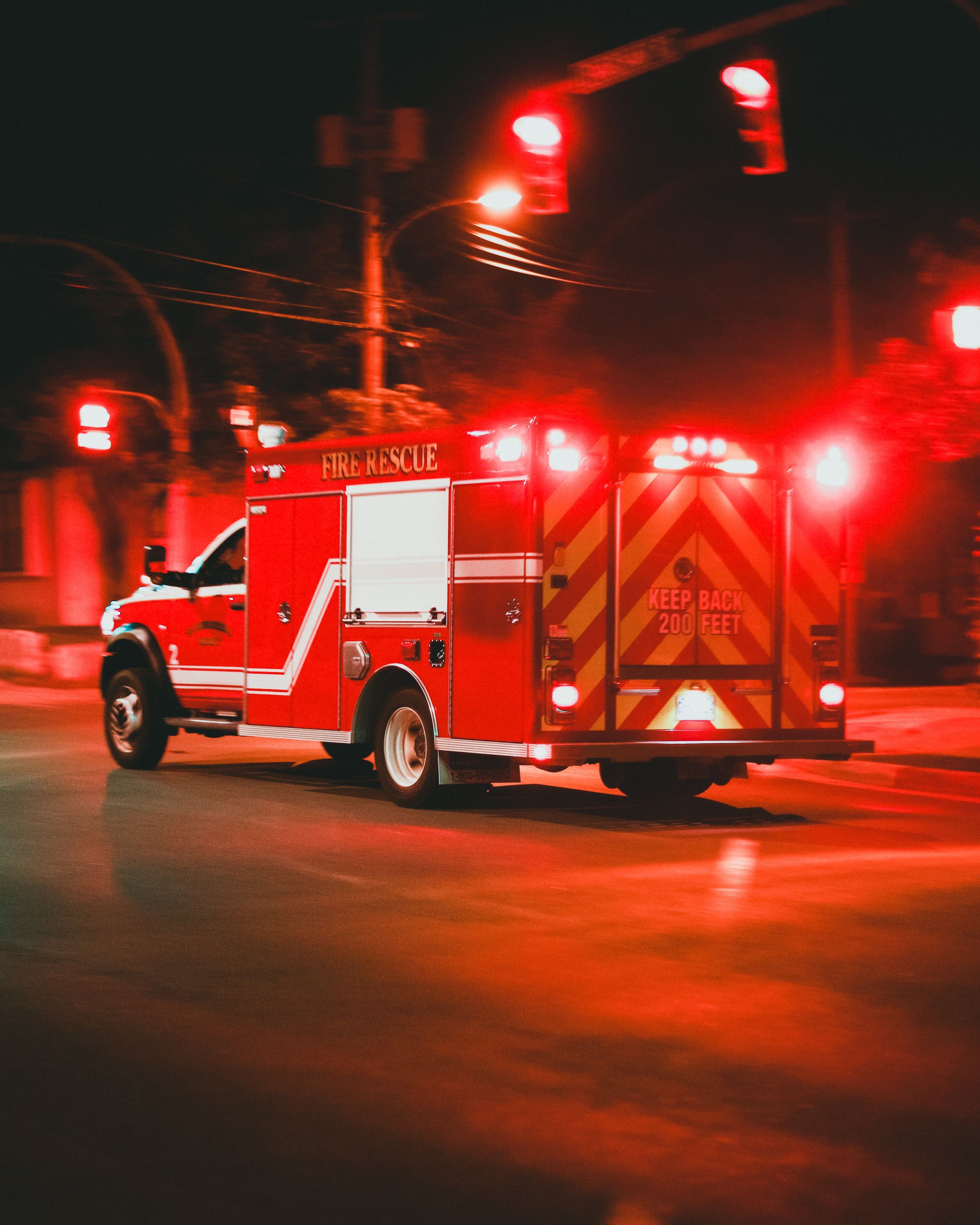 A red fire rescue truck with flashing lights on a dark street at night.