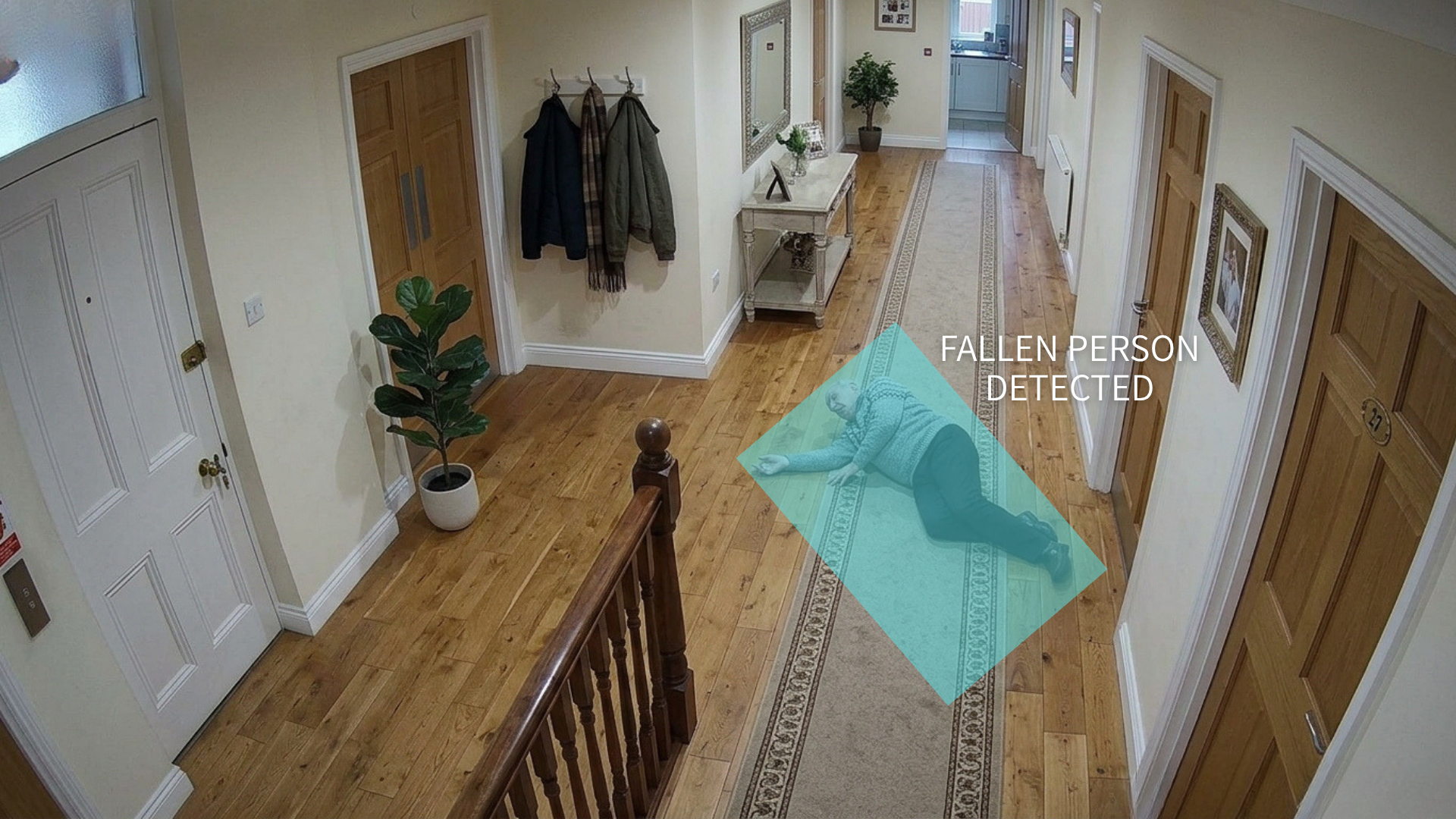 Interior view of a hallway with wooden flooring, multiple doors, a potted plant, a mirror, and a man lying on the carpeted floor with an overlay text indicating 'Fallen Person Detected'.