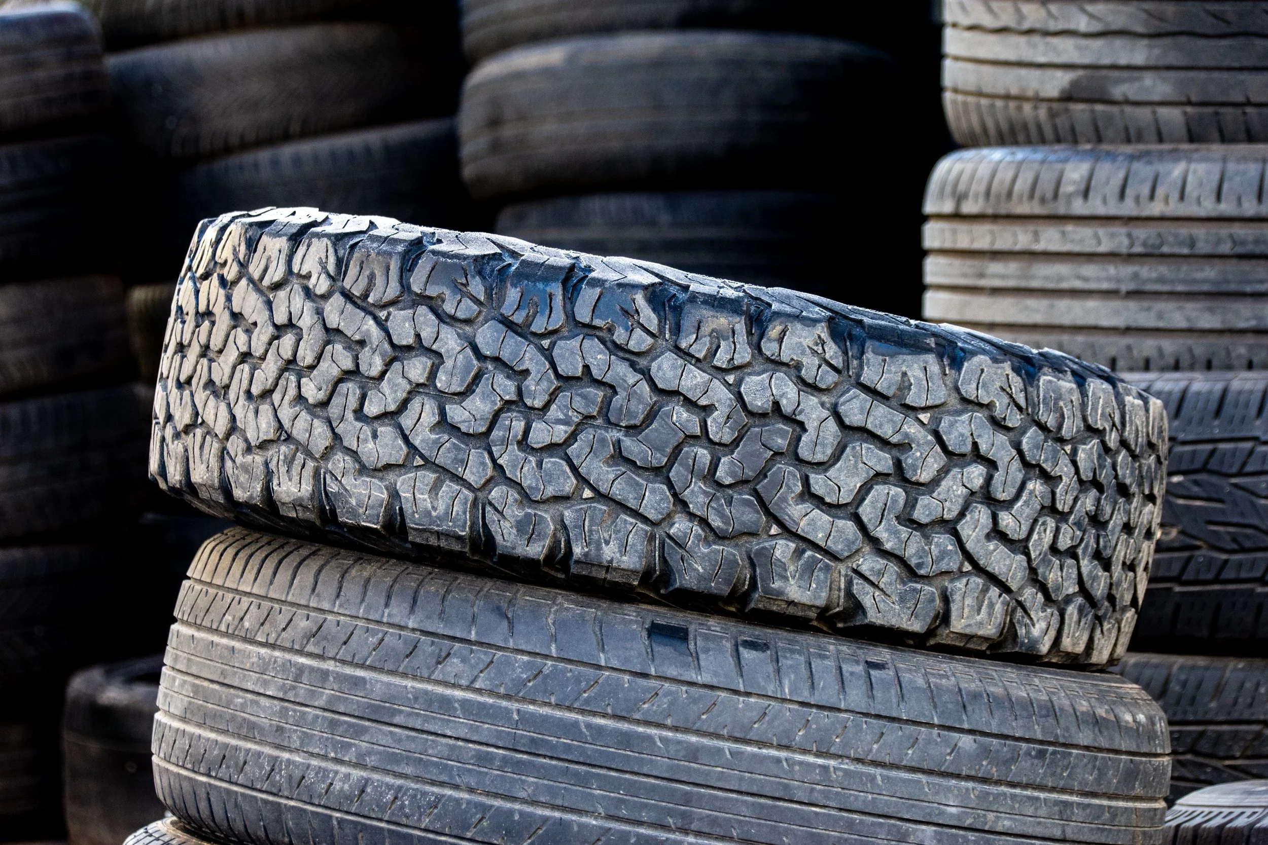 Stacked tires at a tire shop or scrapyard, showing various tread patterns.
