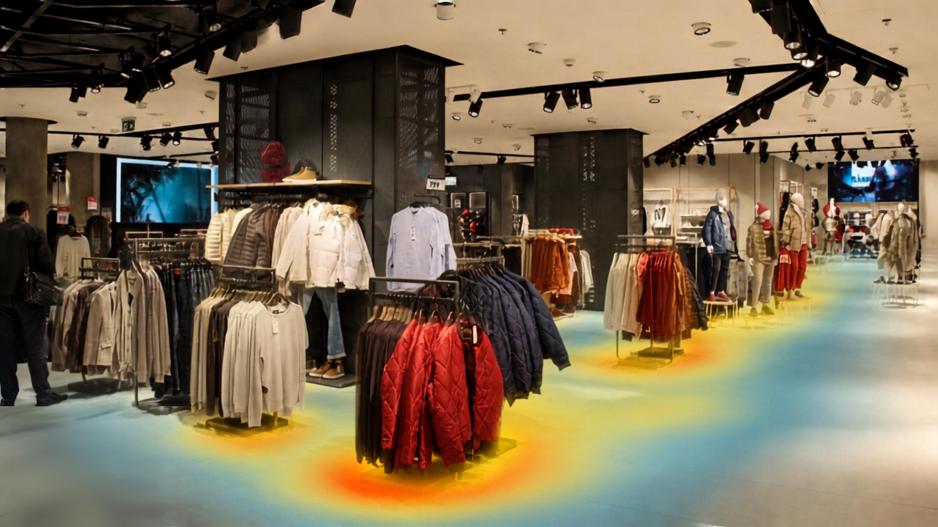 Inside a clothing store with racks of jackets, sweaters, and pants on display, and mannequins dressed in various outfits, under overhead lighting and a heat map overlay showing foot traffic areas.