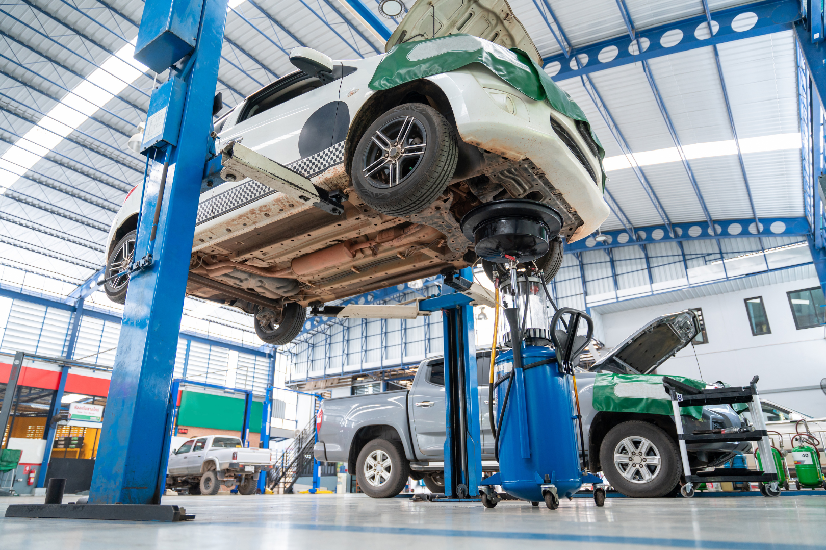 An automobile is lifted on a hydraulic lift in an auto repair shop, with the hood open and various tools nearby.