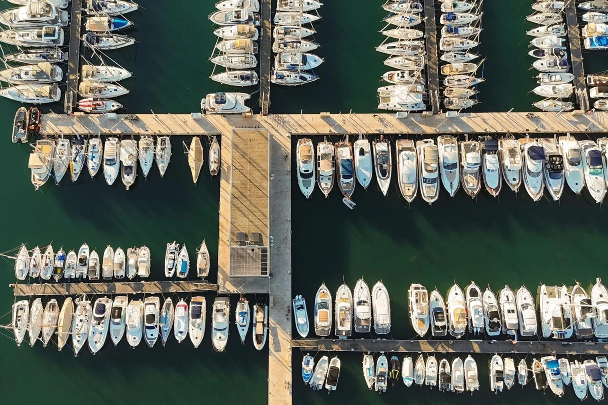 An aerial view of a marina with boats docked on both sides of the wooden piers, situated in calm water.