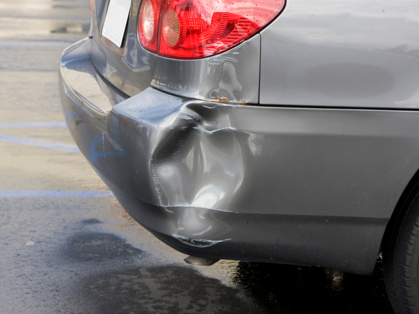 Car with a dented and scratched rear bumper, parked in a parking lot.