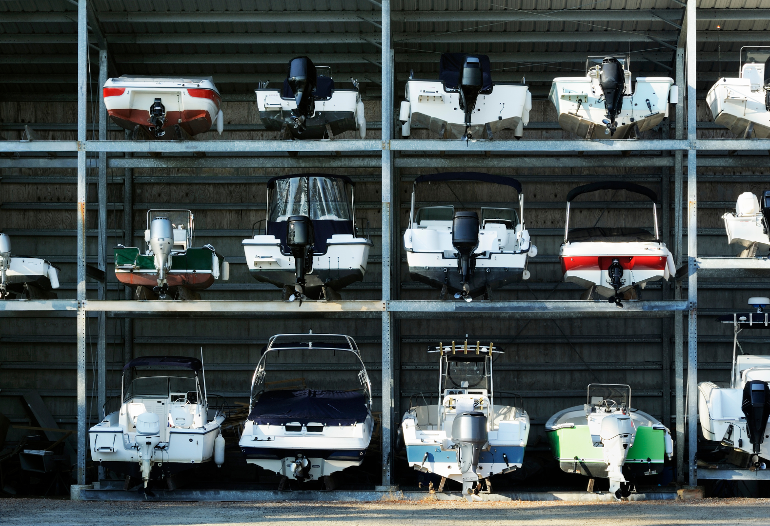 Multiple boats stored on metal racks in a boatyard, with some boats on the ground.