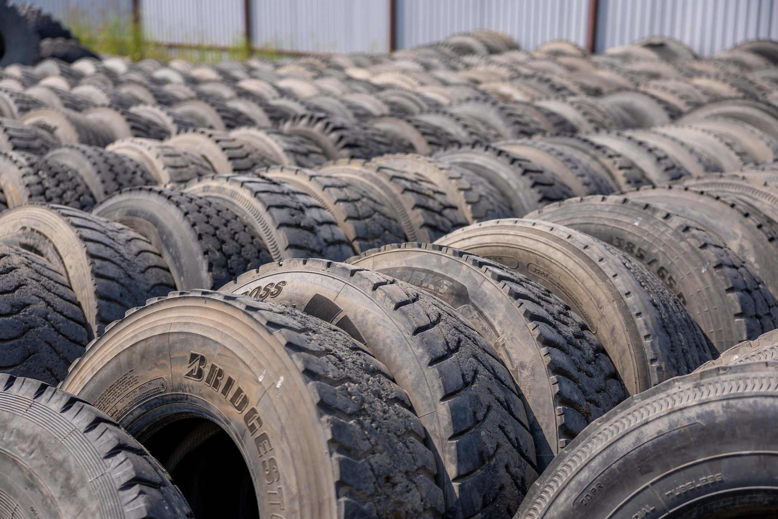 A large pile of used tires stacked outdoors behind a fence.