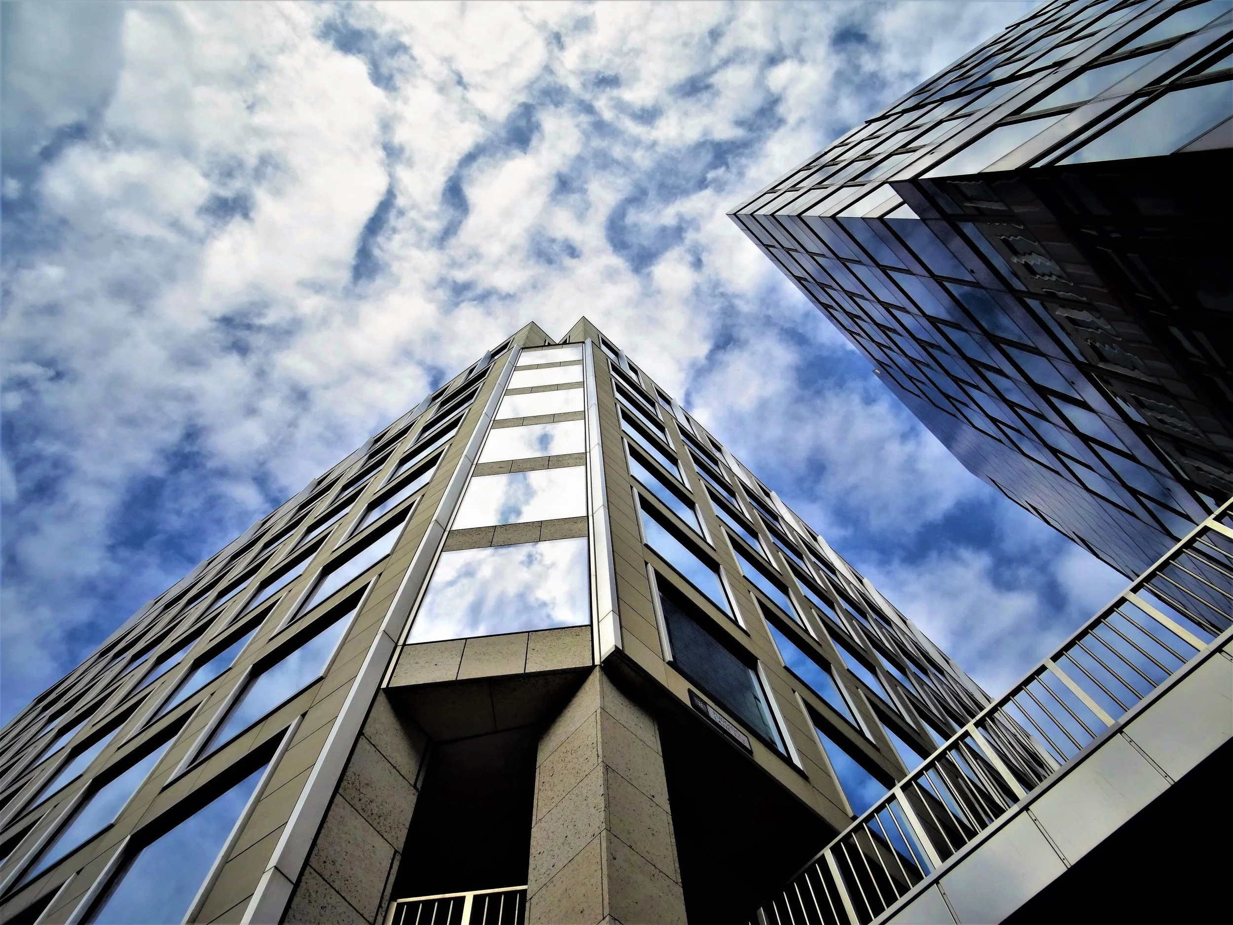 Looking up at modern high-rise buildings with glass facades against a partly cloudy sky.