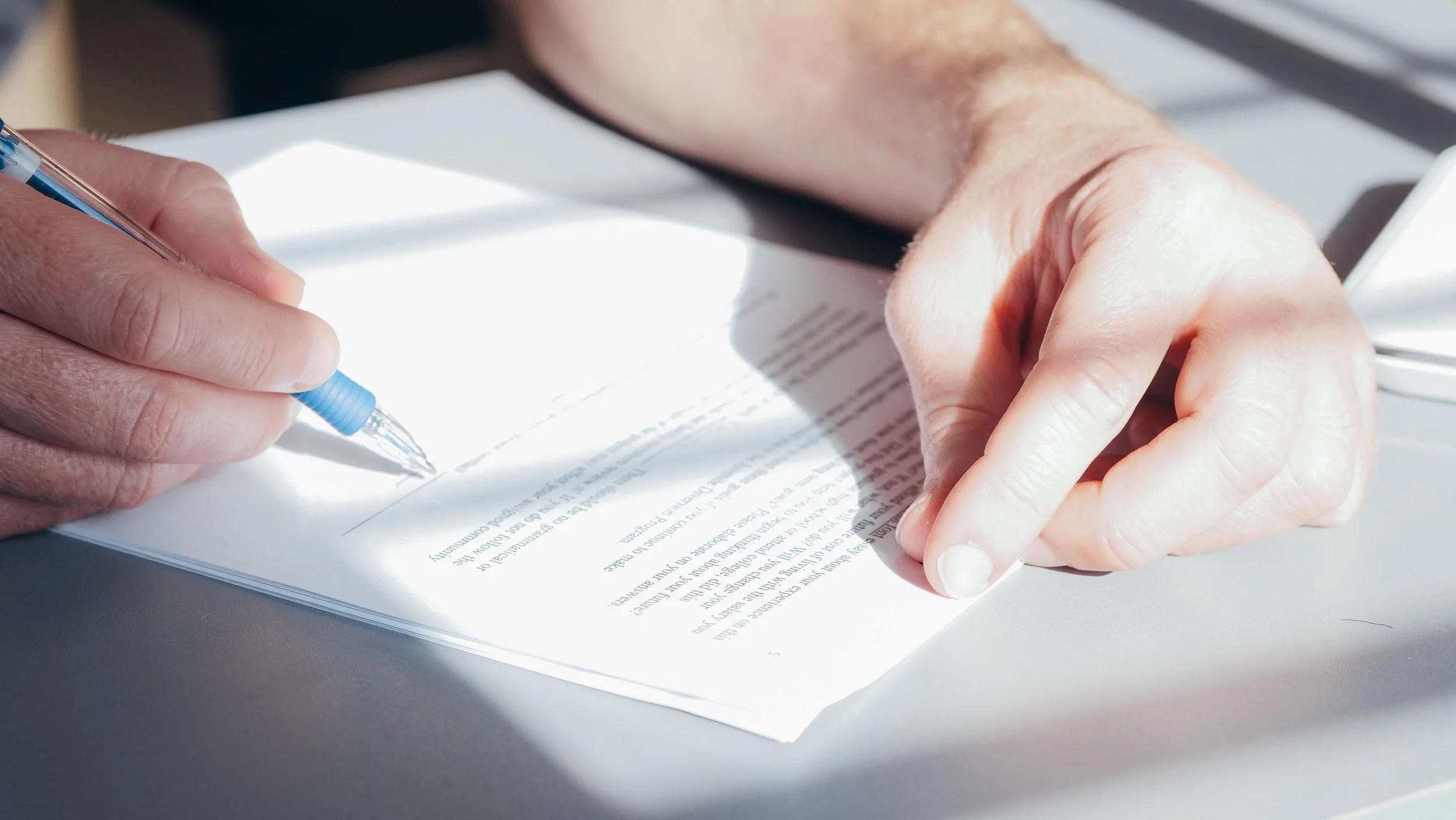 Close-up of a person signing a document with a blue pen, focusing on their hands and the paper.