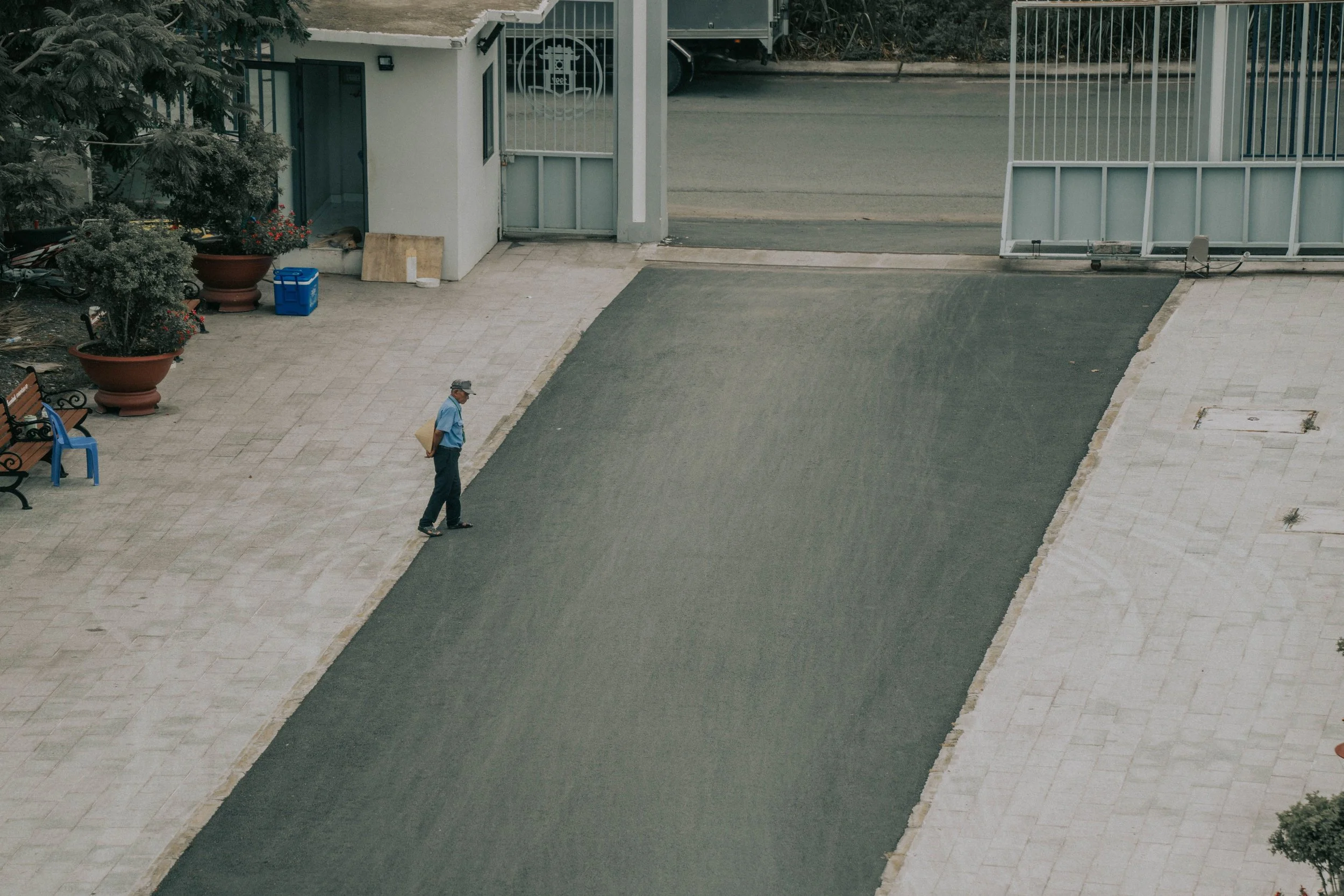 A security gate is partially open while a security guard walks across the driveway.