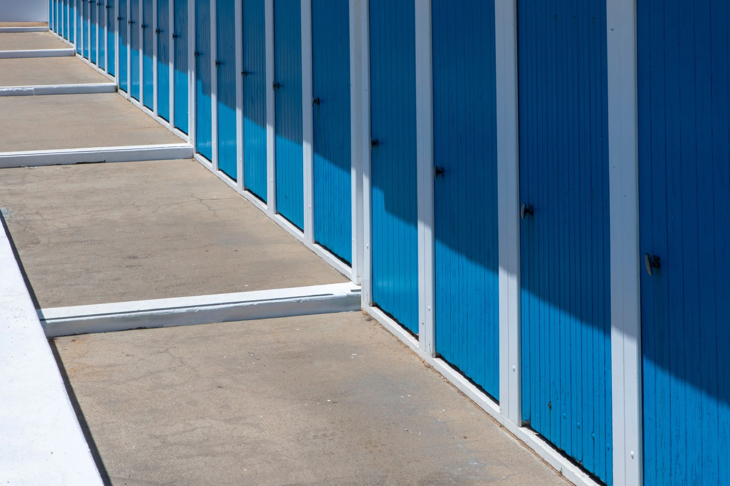 Row of blue lockers with handles, running along a beige sidewalk with white borders
