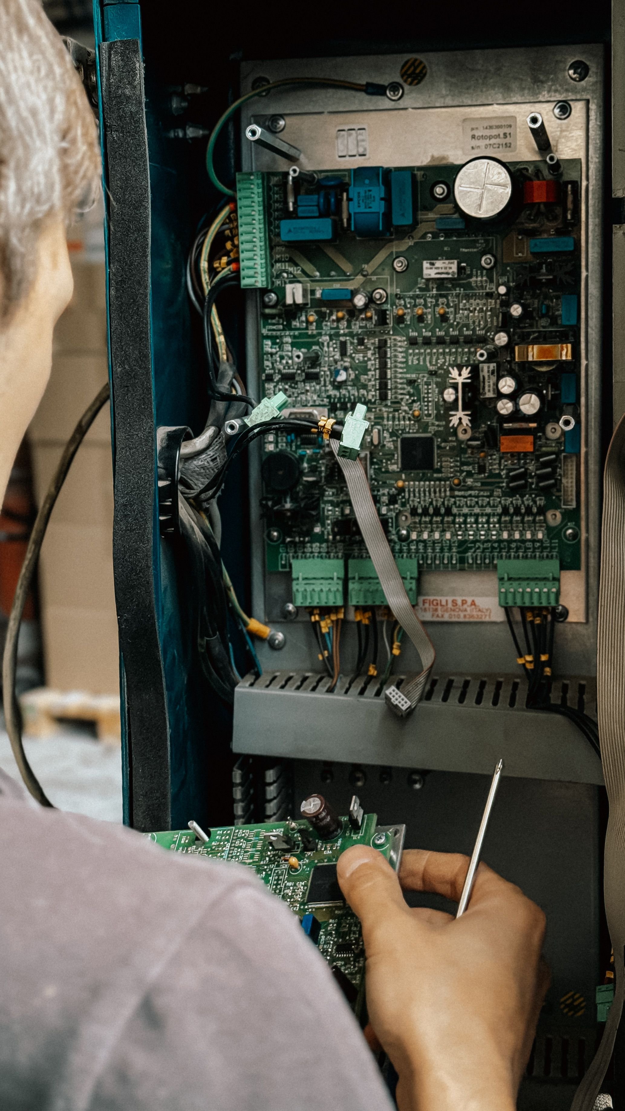 Person repairing or assembling an electronic circuit inside a metal housing, using a screwdriver to work on the circuit board.