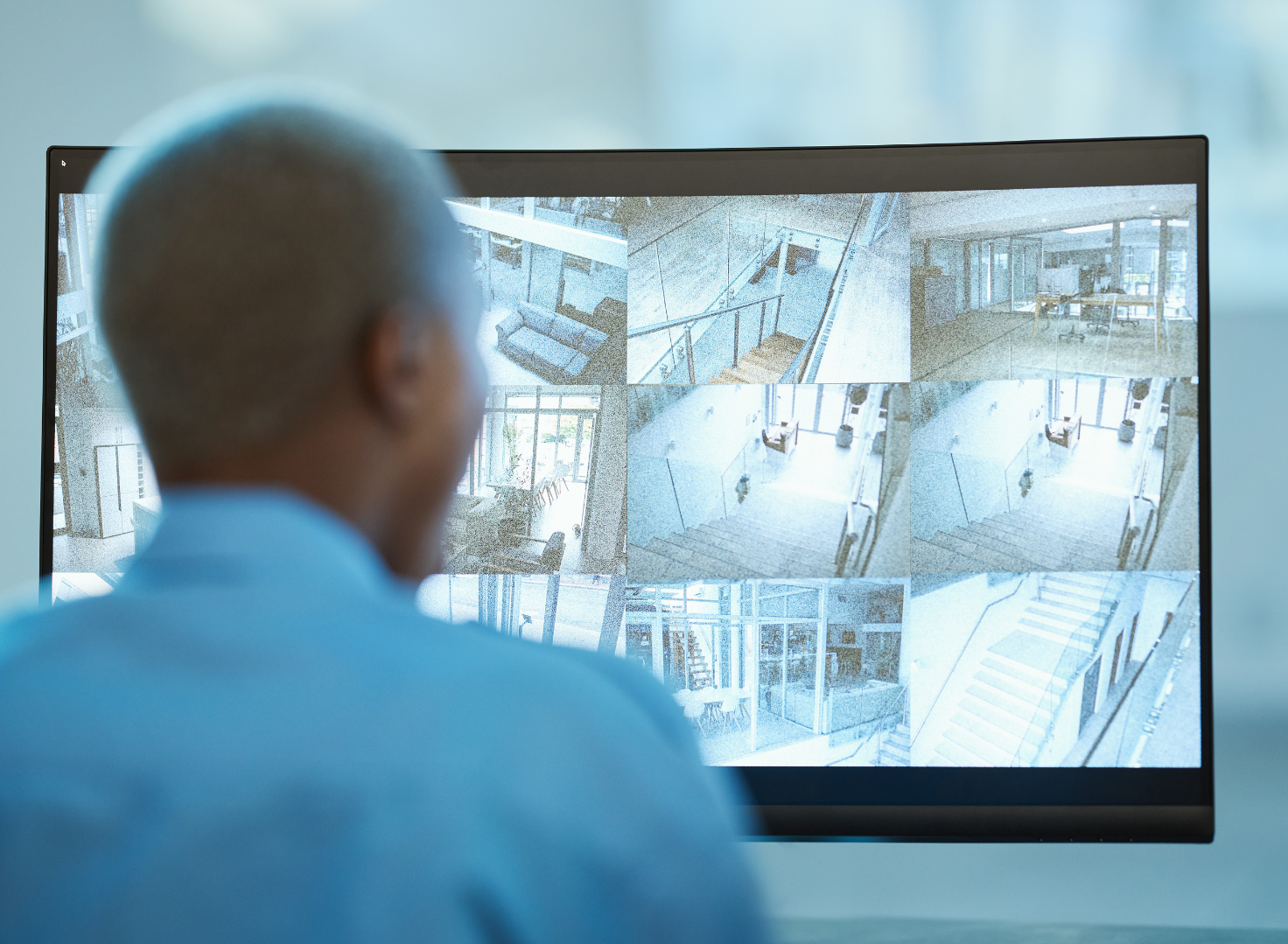 A person looking at surveillance camera monitor showing multiple live feeds of building interior spaces.