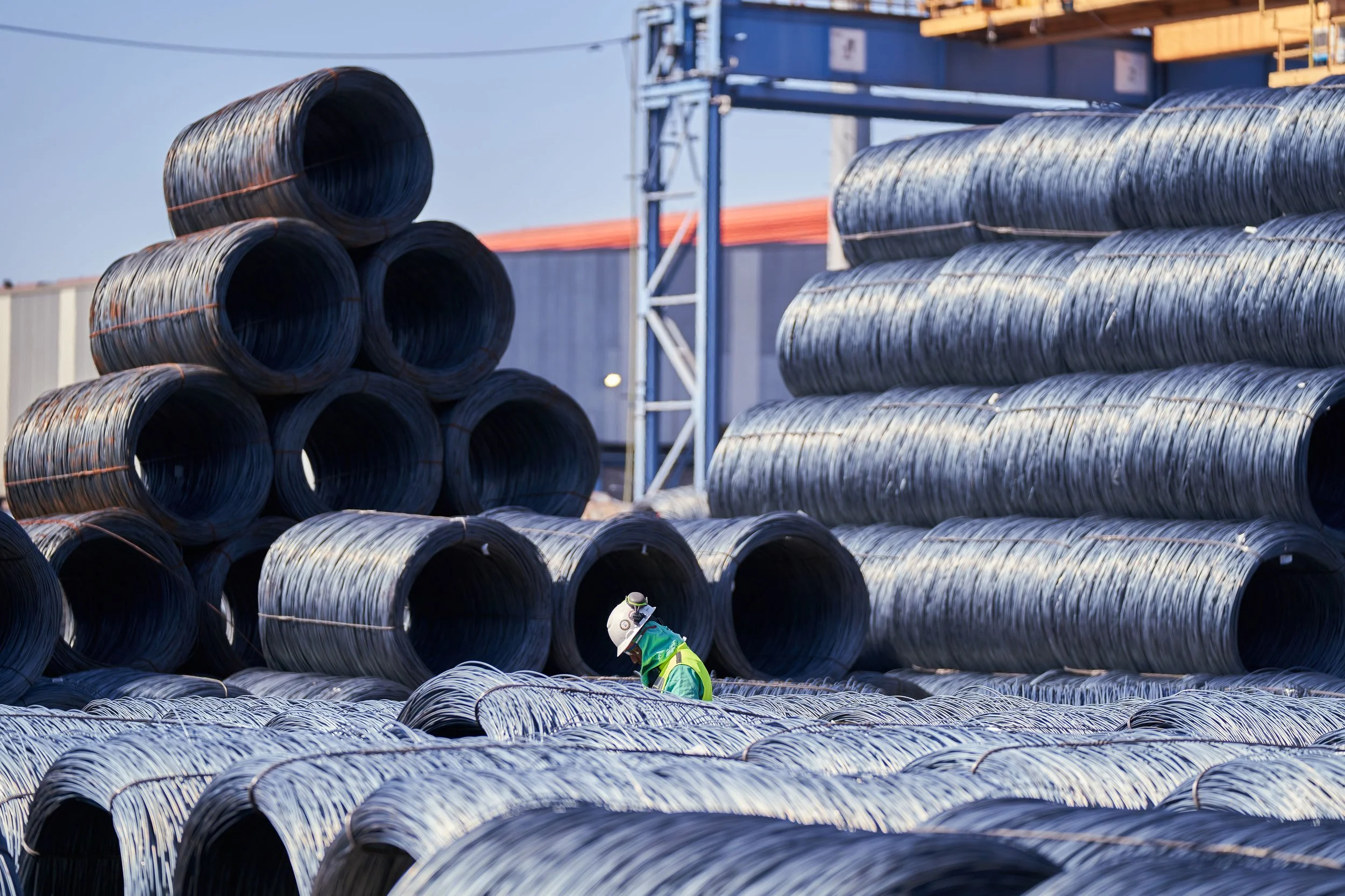 Construction worker in safety gear inspecting large rolls of steel rebar at a construction site.