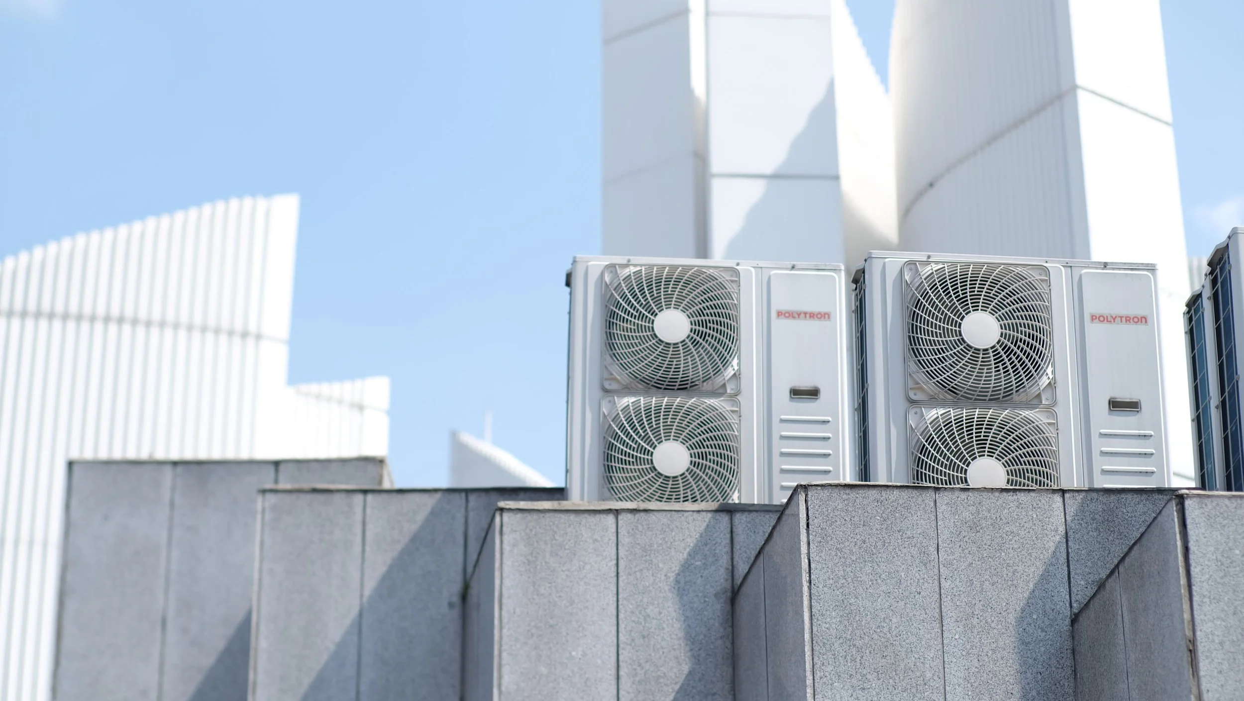 Air conditioning units on a rooftop with a cityscape and blue sky in the background.