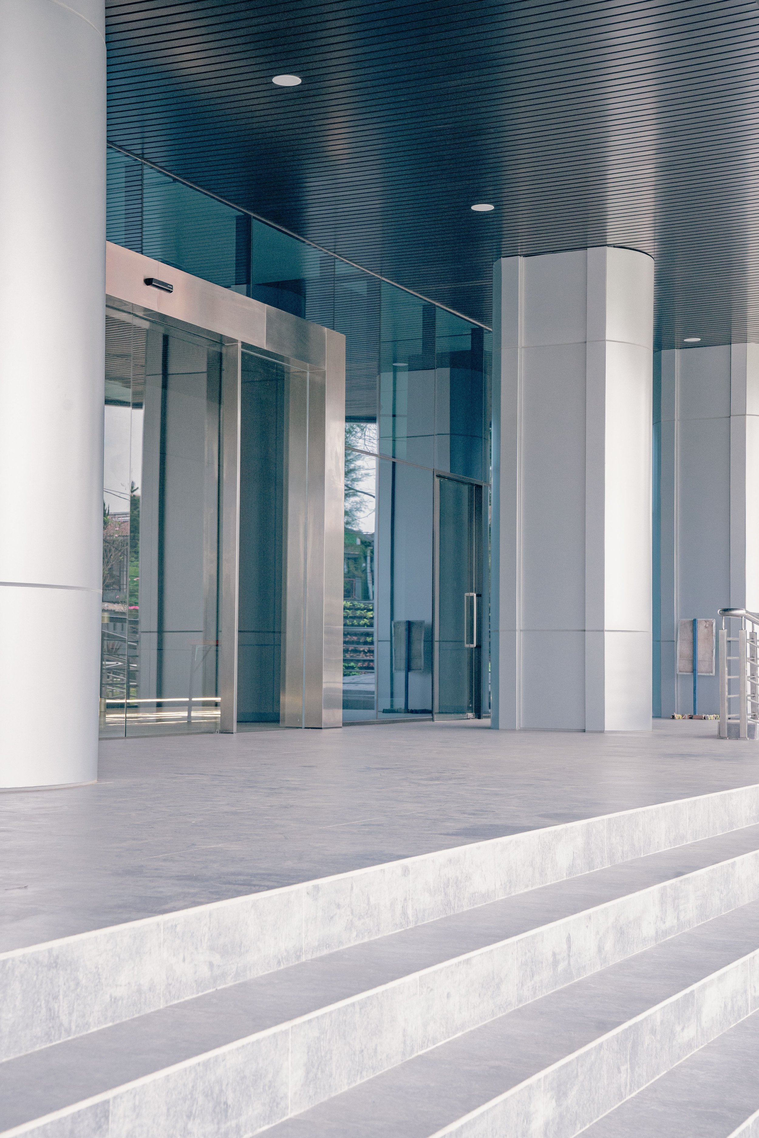 Modern building entrance with glass doors, white columns, and concrete steps leading up to the entrance.