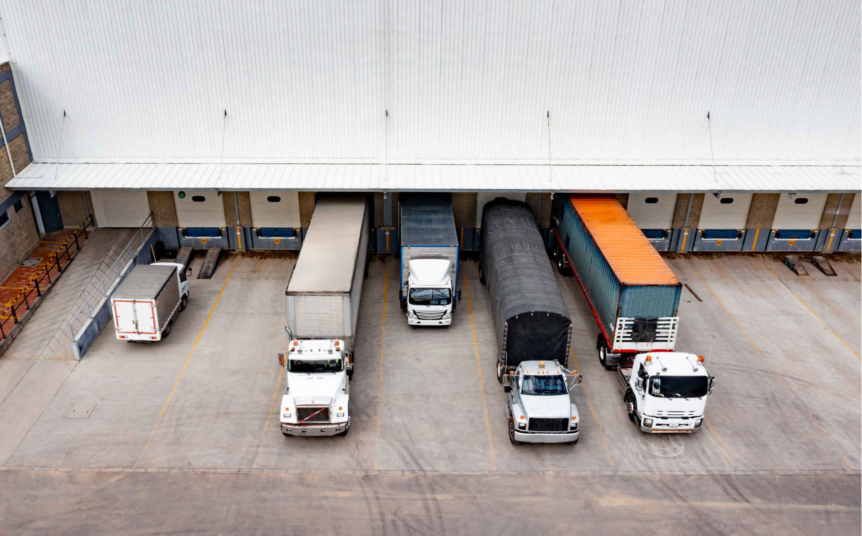 Multiple trucks and trailers parked at loading docks outside a warehouse