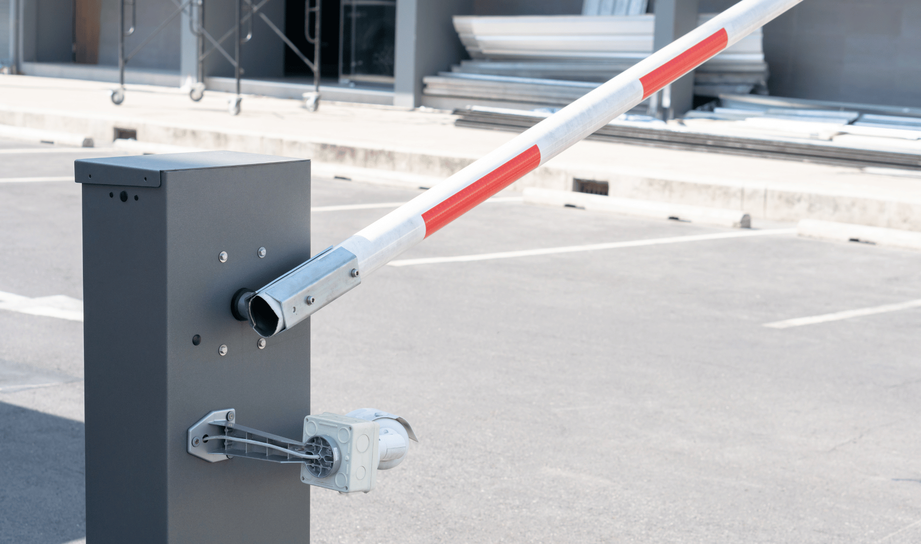 Automated parking barrier gate arm in a parking lot, with a background of empty parking spaces and a building under renovation.