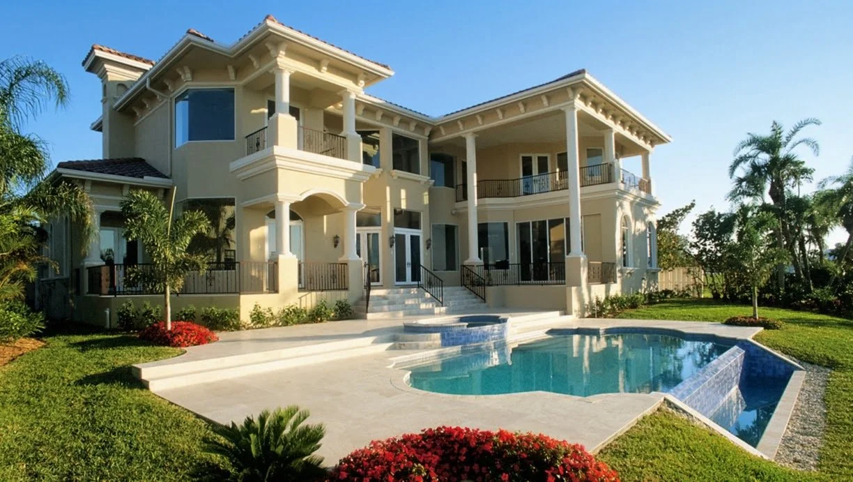 Large luxury house with multiple balconies and a backyard pool surrounded by green lawn and trees under a clear blue sky.