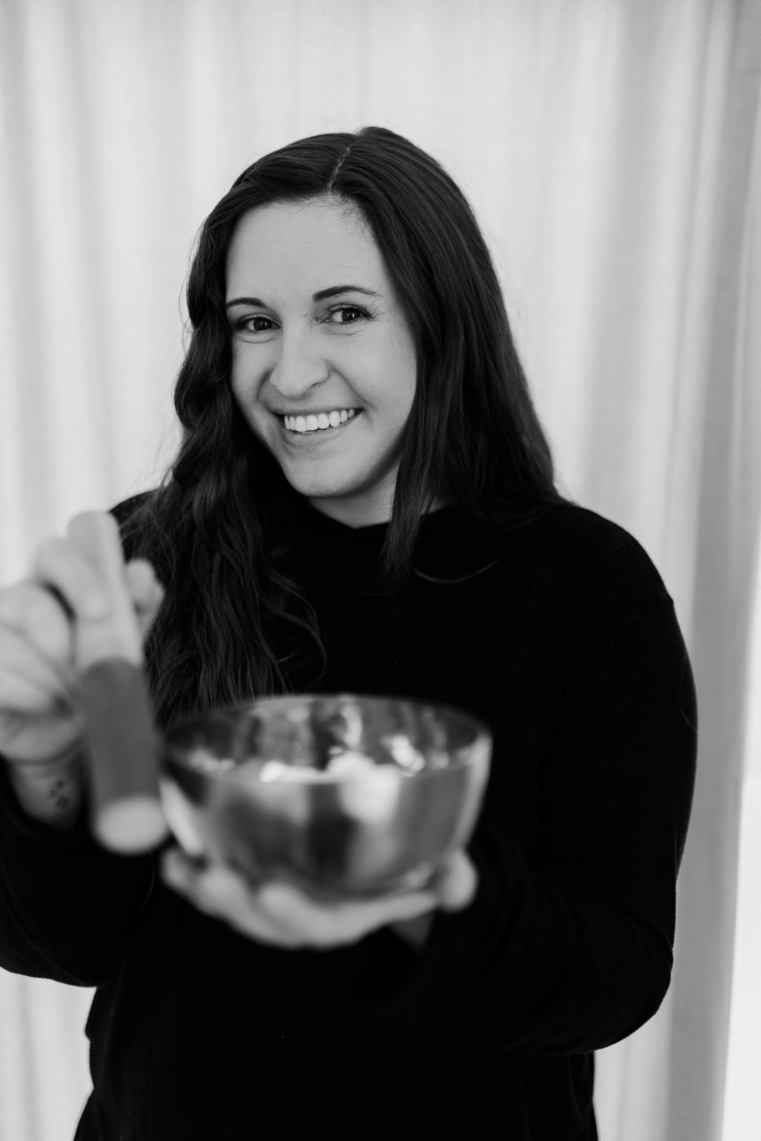 A woman with long dark hair smiling and holding a Tibetan bowl.
