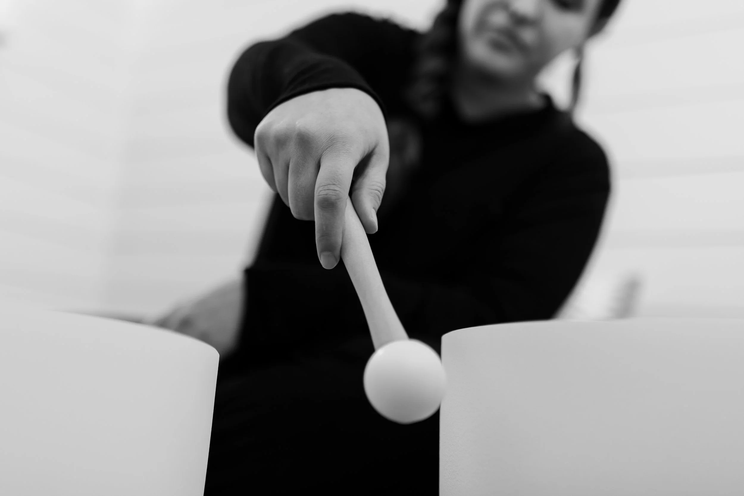 A woman with a braid playing a crystal singing bowl with a mallet.
