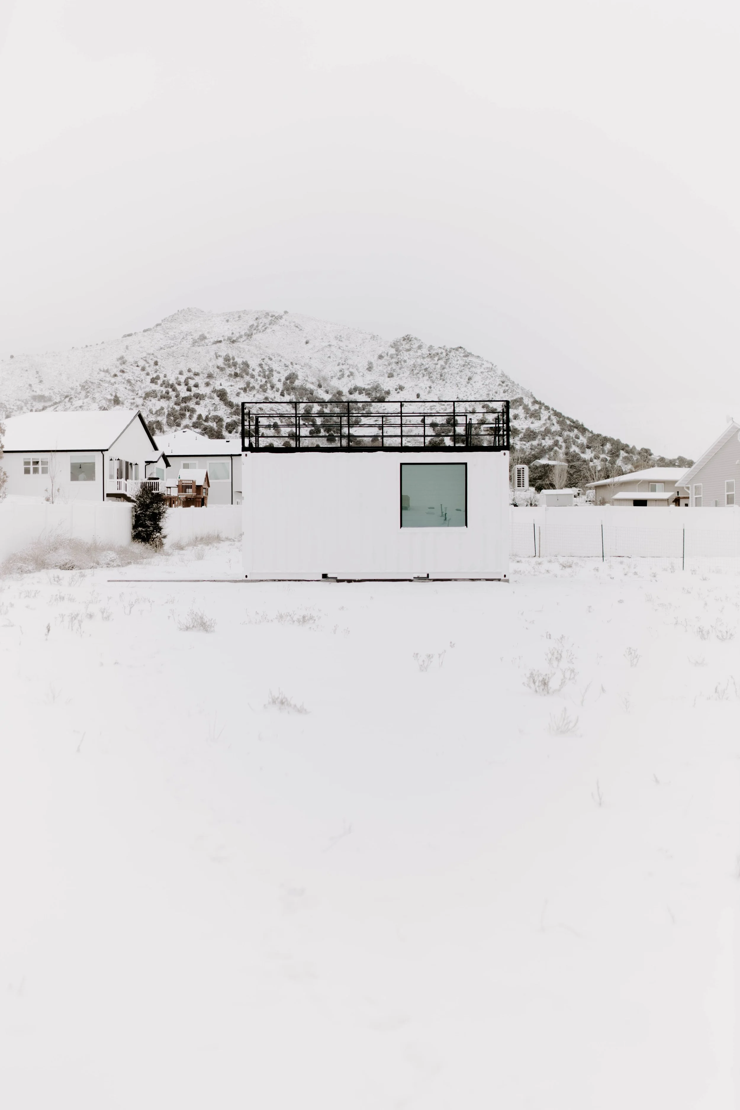 A snowy landscape with a modern white studio and a mountain in the background.