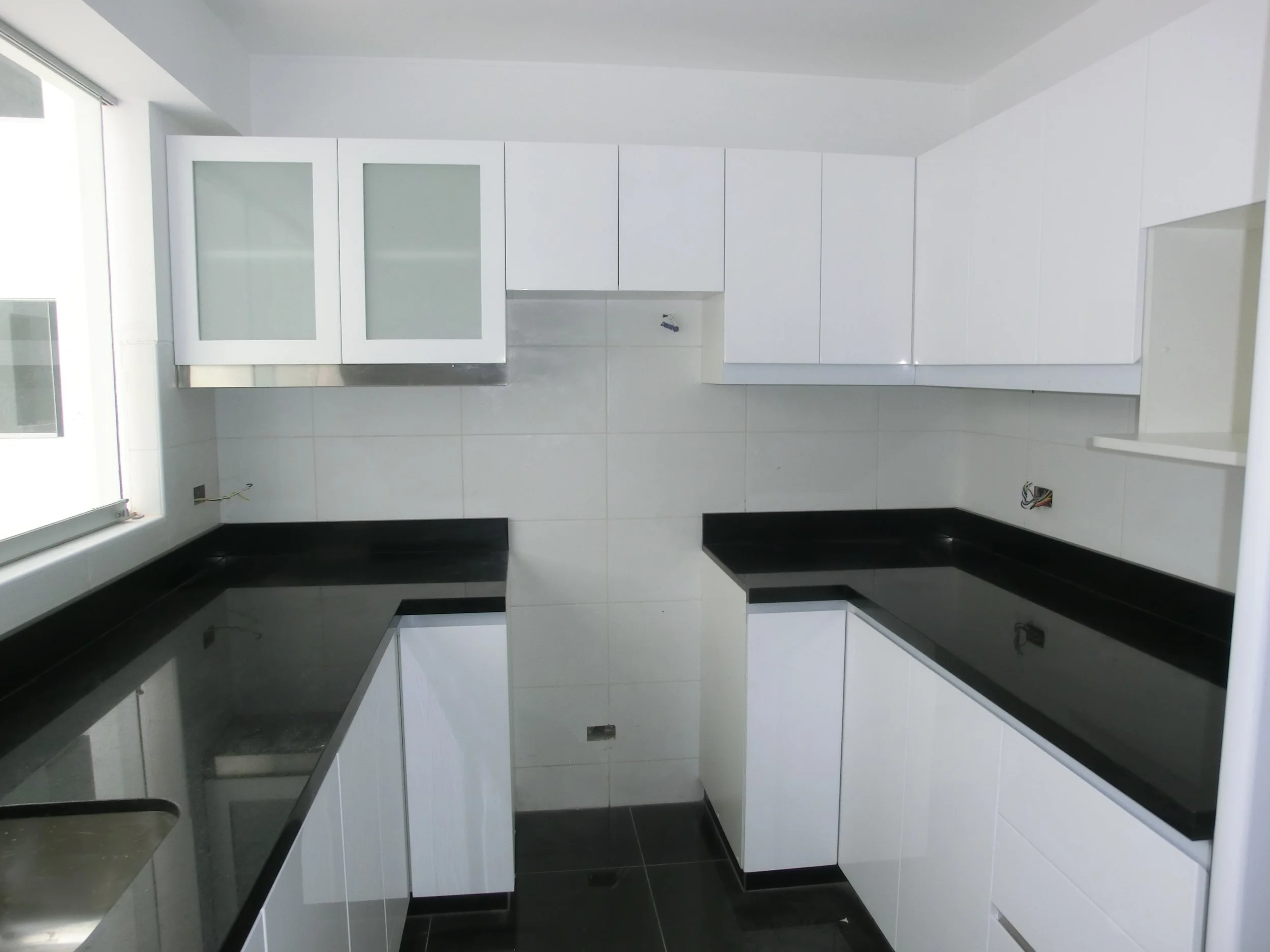 Cocina moderna con gabinetes blancos, tablero  de granito color negro, puertas de melamine con vidrio y cajones corredizas a la izquierda ventana sistema nova corrediza