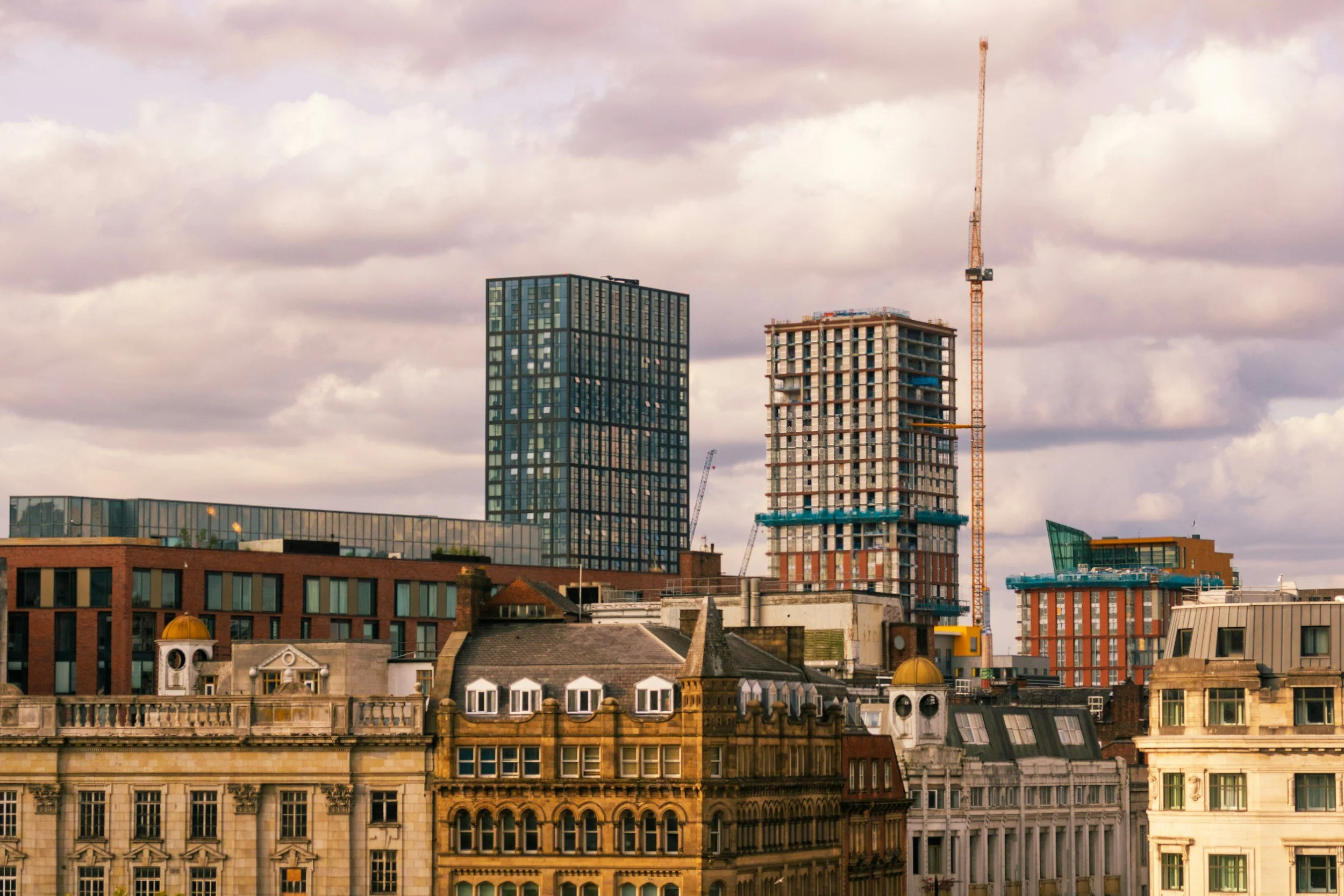 City skyline featuring various buildings under a cloudy sky, including a high-rise under construction with a crane.