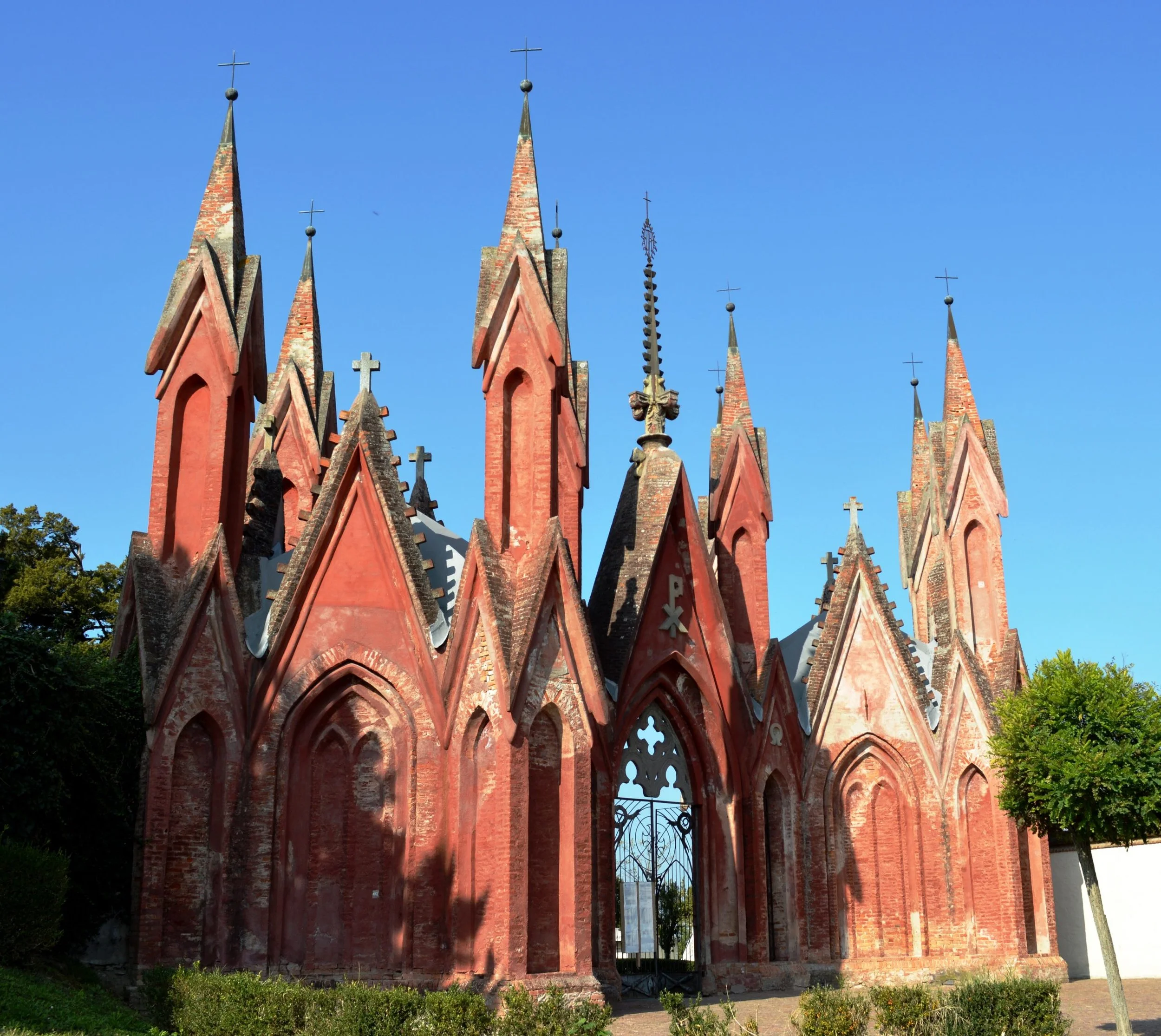 Chiesa con torri e guglie in architettura gotica di colore rosso, con croci sulla cima delle torri, sotto un cielo blu.