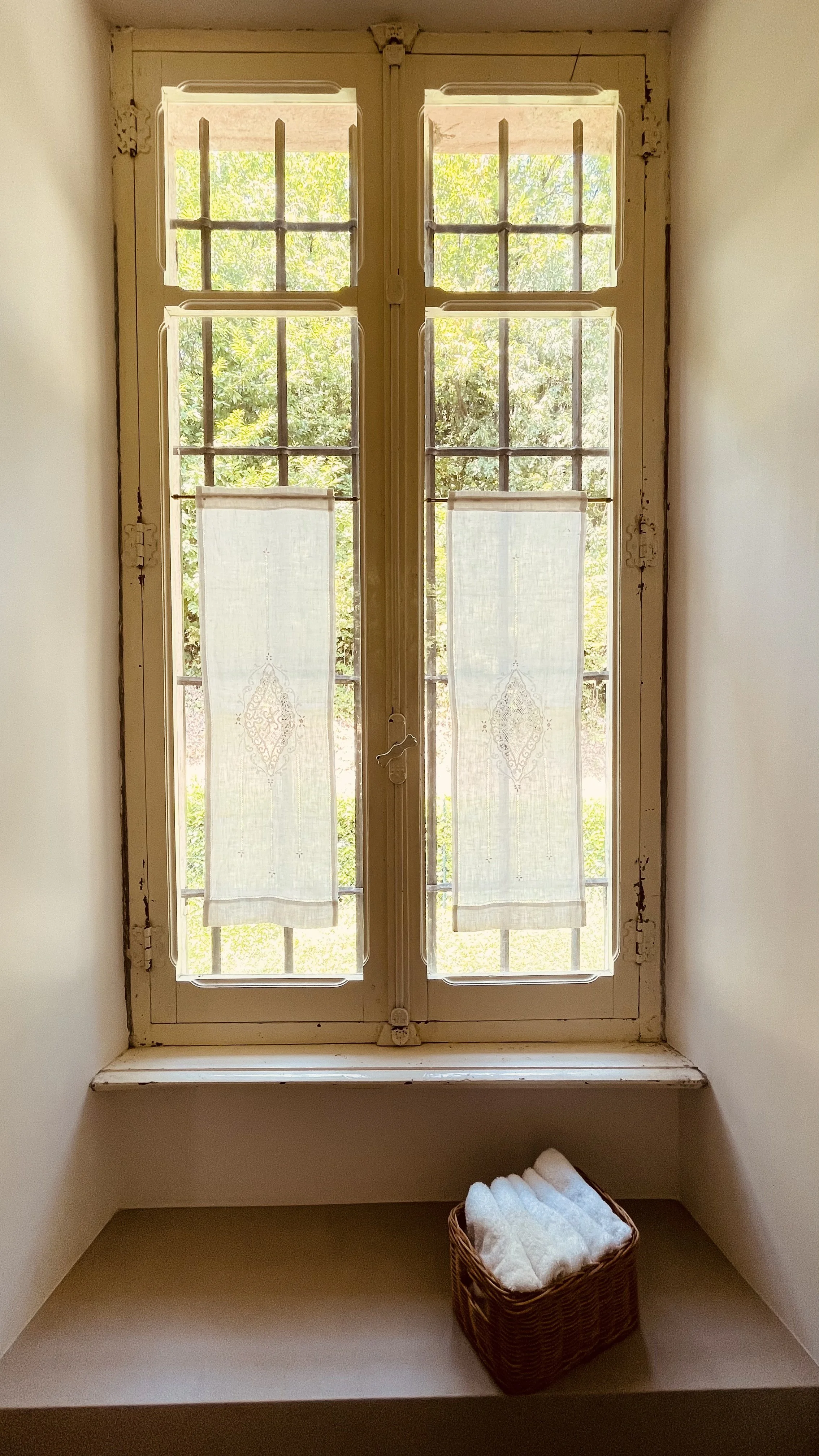 Historic garden window with linen curtains in the Fresco Rooms bathroom at Villa Oberti in Piedmont