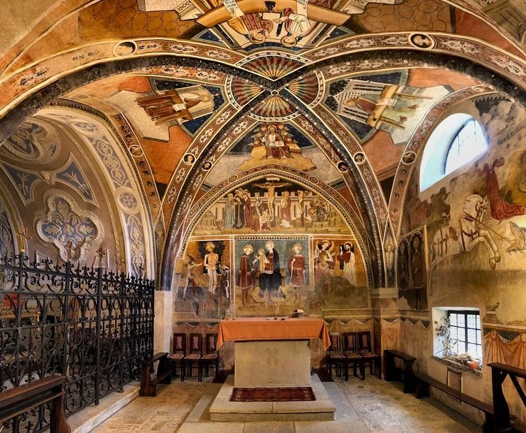Interno di una chiesa o cappella con affreschi religiosi sulle pareti e sul soffitto, con un altare al centro e sedie ai lati.