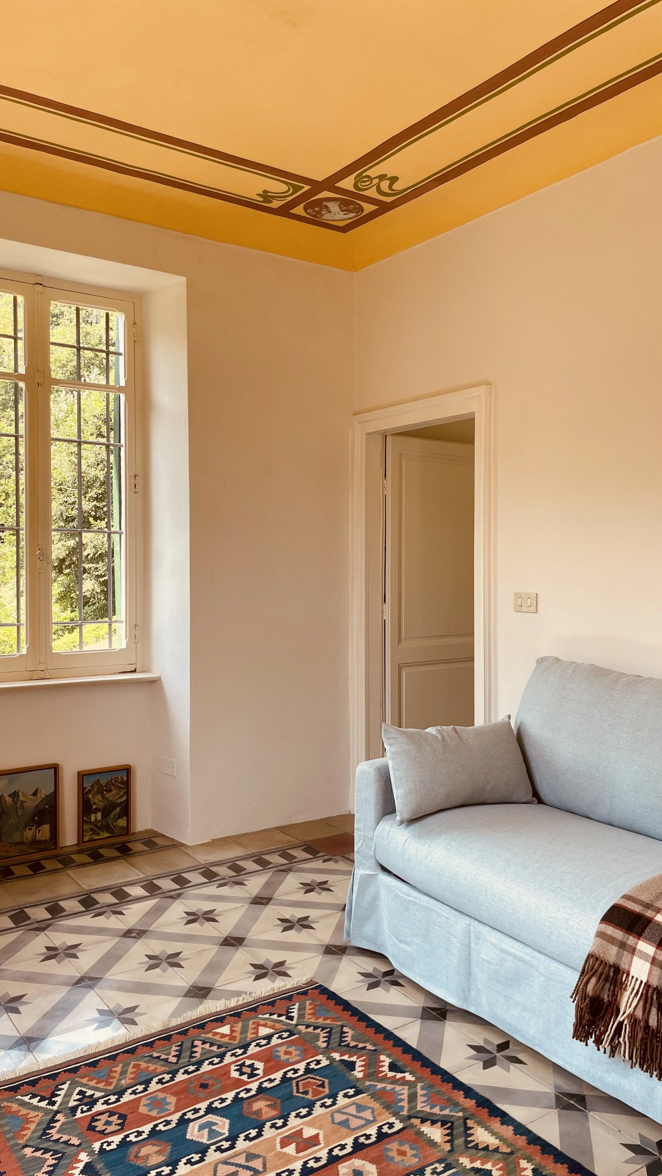 Private study with blue sofa, painted ceiling and garden window at Villa Oberti, a historic villa near the Langhe