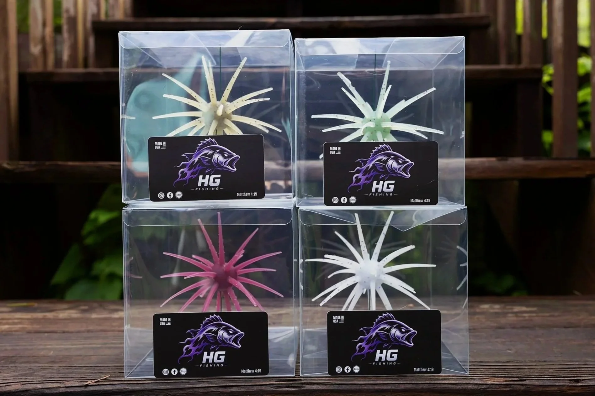 Four boxes containing colorful fishing lures in clear packaging, placed on a wooden surface outdoors.