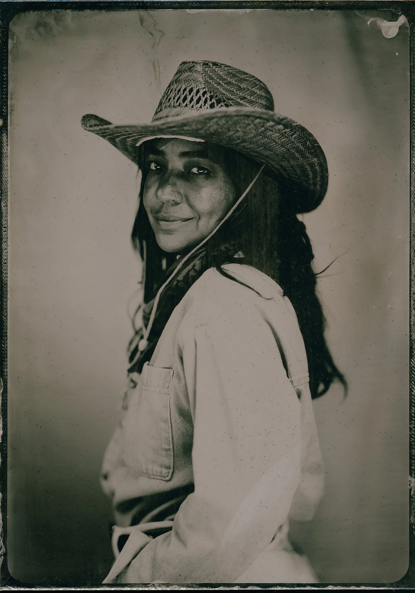 Portrait en noir et blanc d'une femme portant un chapeau de paille large et un vêtement blanc, regardant vers l'objectif avec un léger sourire.