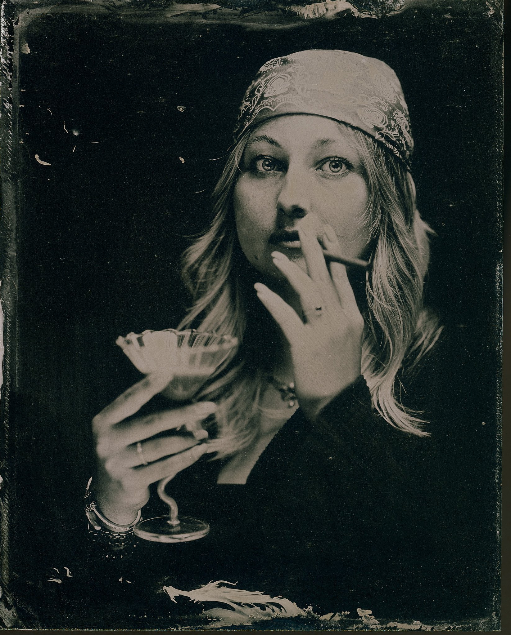 Un portrait noir et blanc d'une femme portant un bandana, tenant une coupe de cocktail avec une paille, regardant vers l'objectif, ambiance artistique.