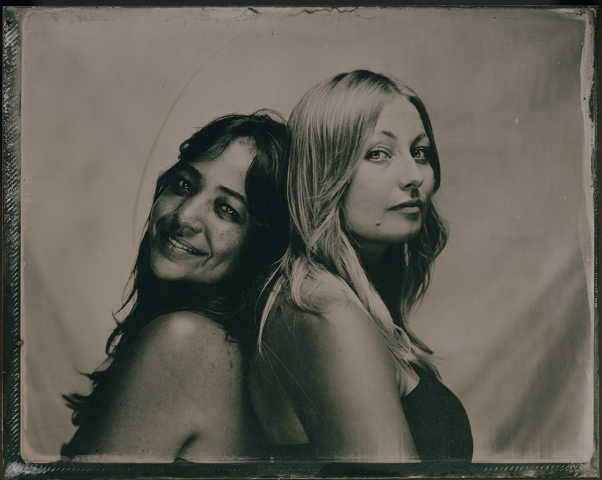 Photographie en noir et blanc de deux femmes, l'une avec des cheveux foncés et l'autre avec des cheveux blonds, posant côte à côte avec des expressions faciales différentes.